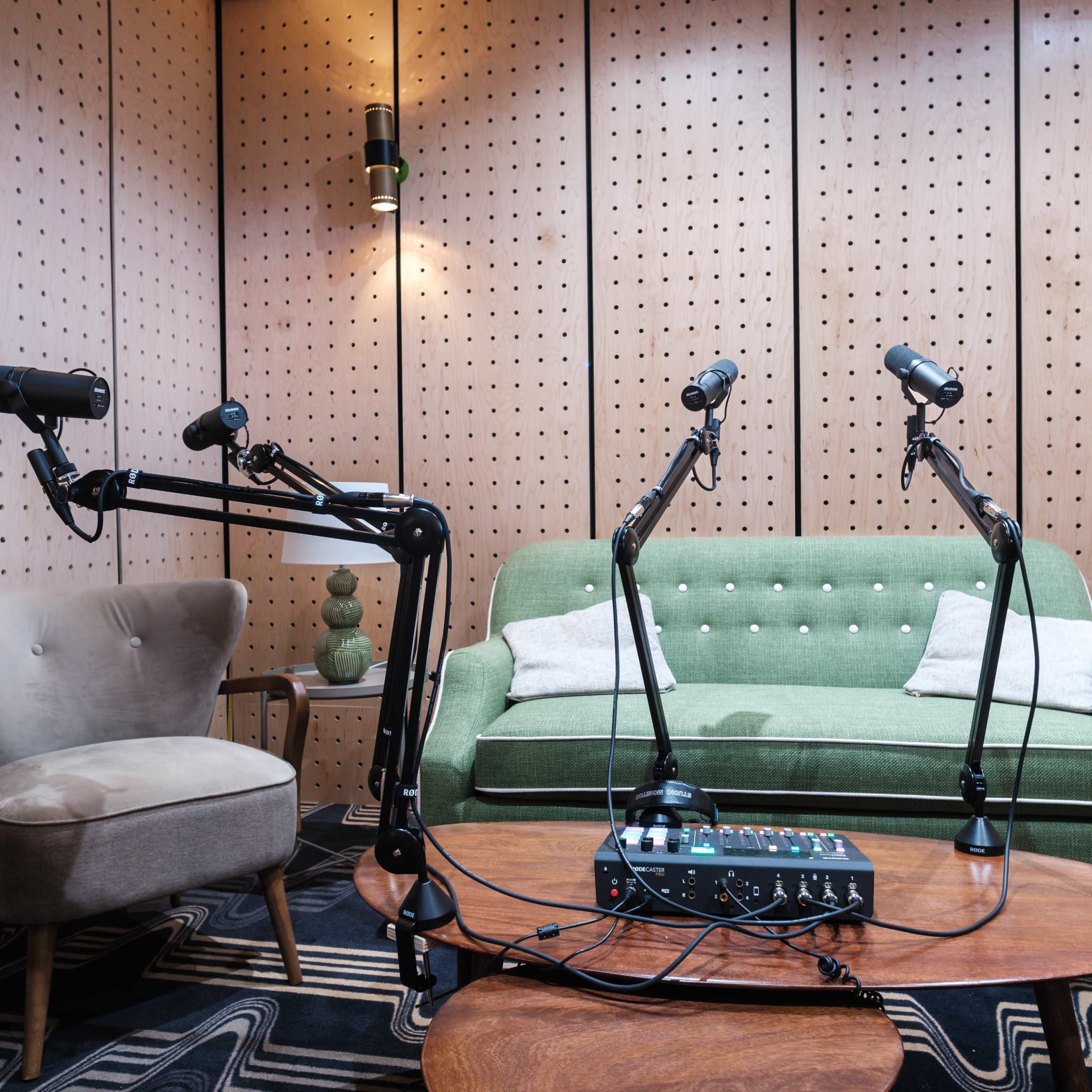 A sound studio with two microphones on adjustable arms positioned near a green sofa and a wooden coffee table.