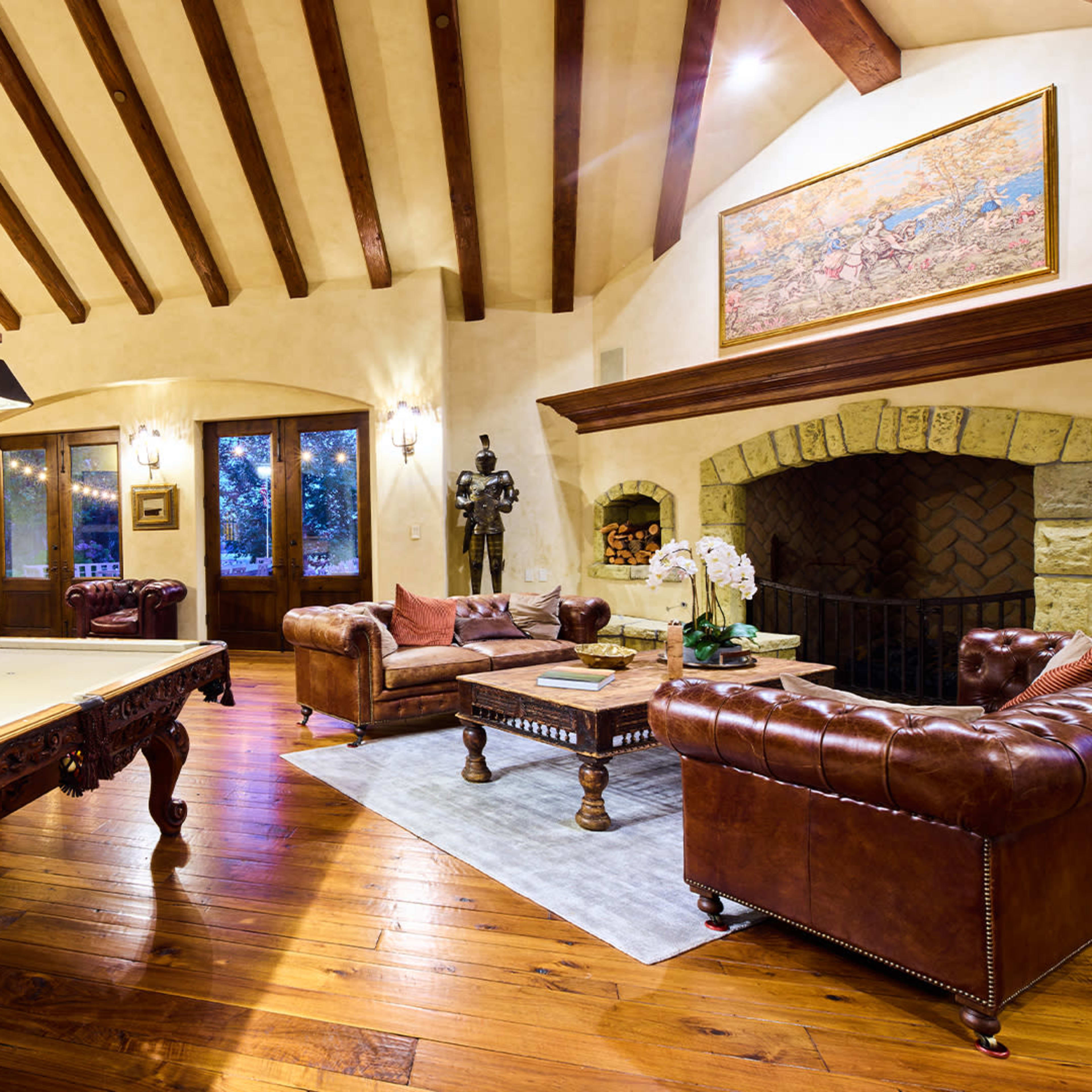 A spacious living room with a pool table, leather sofas, a fireplace, and wooden beams on the ceiling.