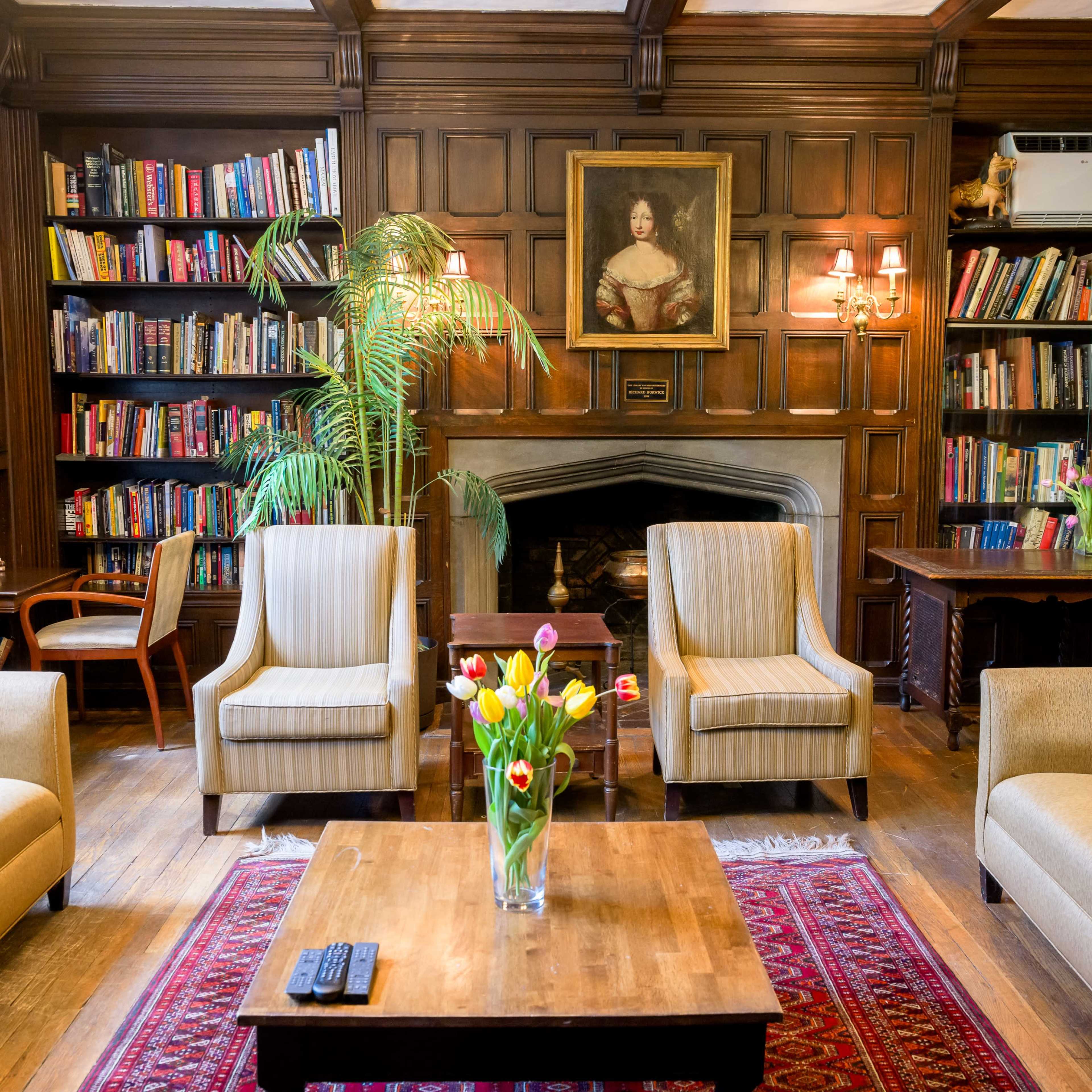 A cozy library with wooden paneling, equipped with bookshelves, comfortable seating, and a decorative flower arrangement on a coffee table.
