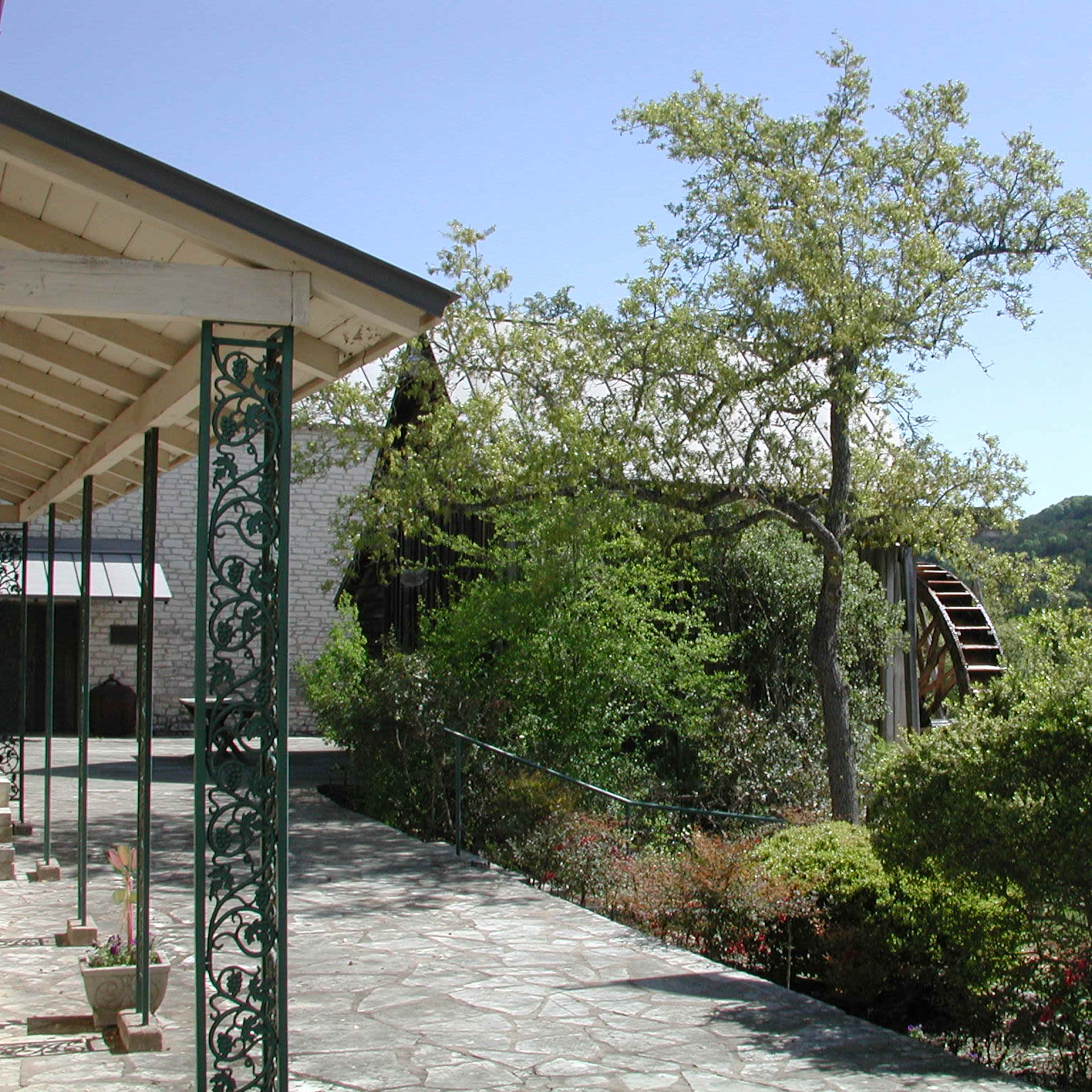 A stone pathway leading to a building with an American and a Texas flag flying, surrounded by greenery and hills in the background.