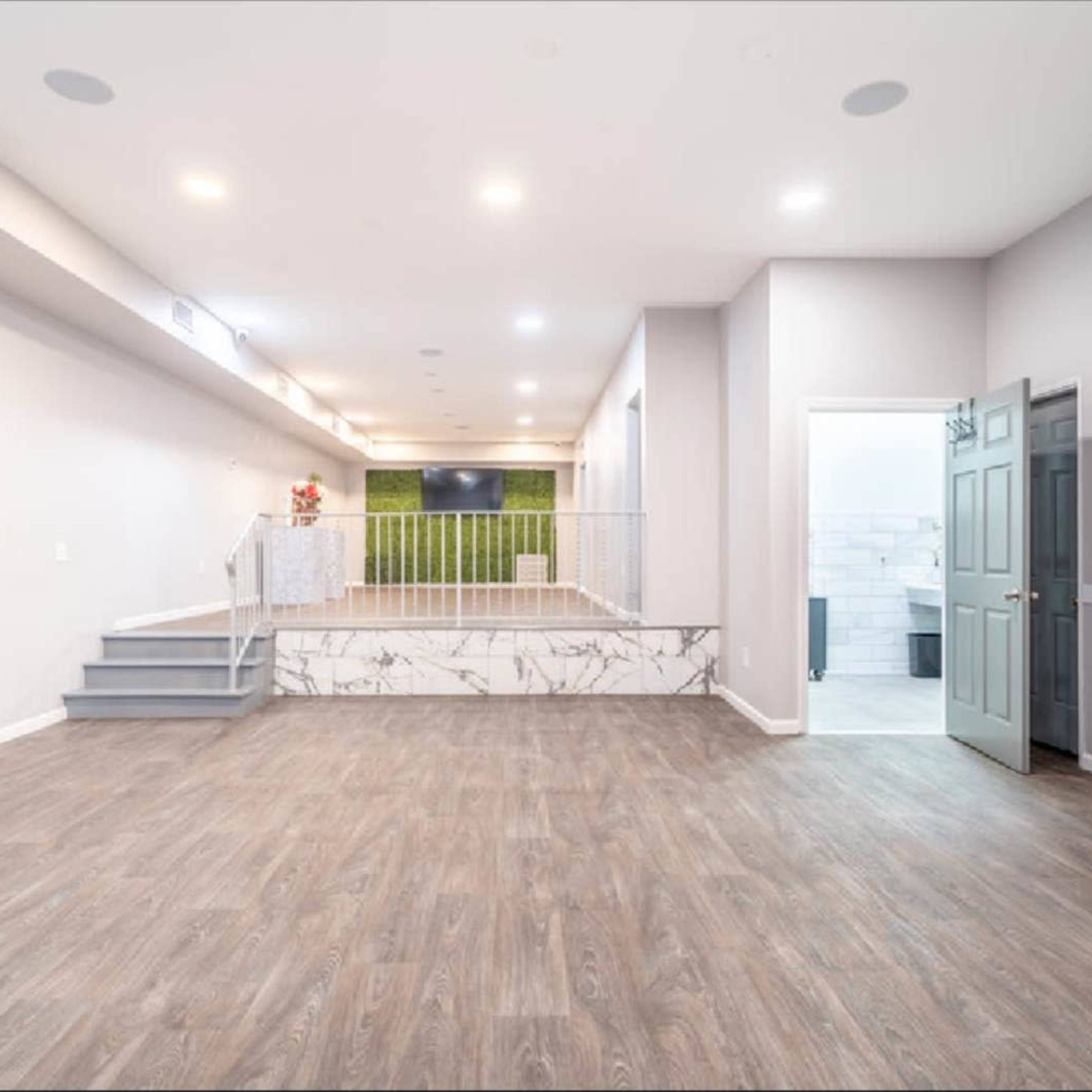 A spacious, modern interior living area with light-colored walls, wooden flooring, and a set of stairs leading to a raised platform.