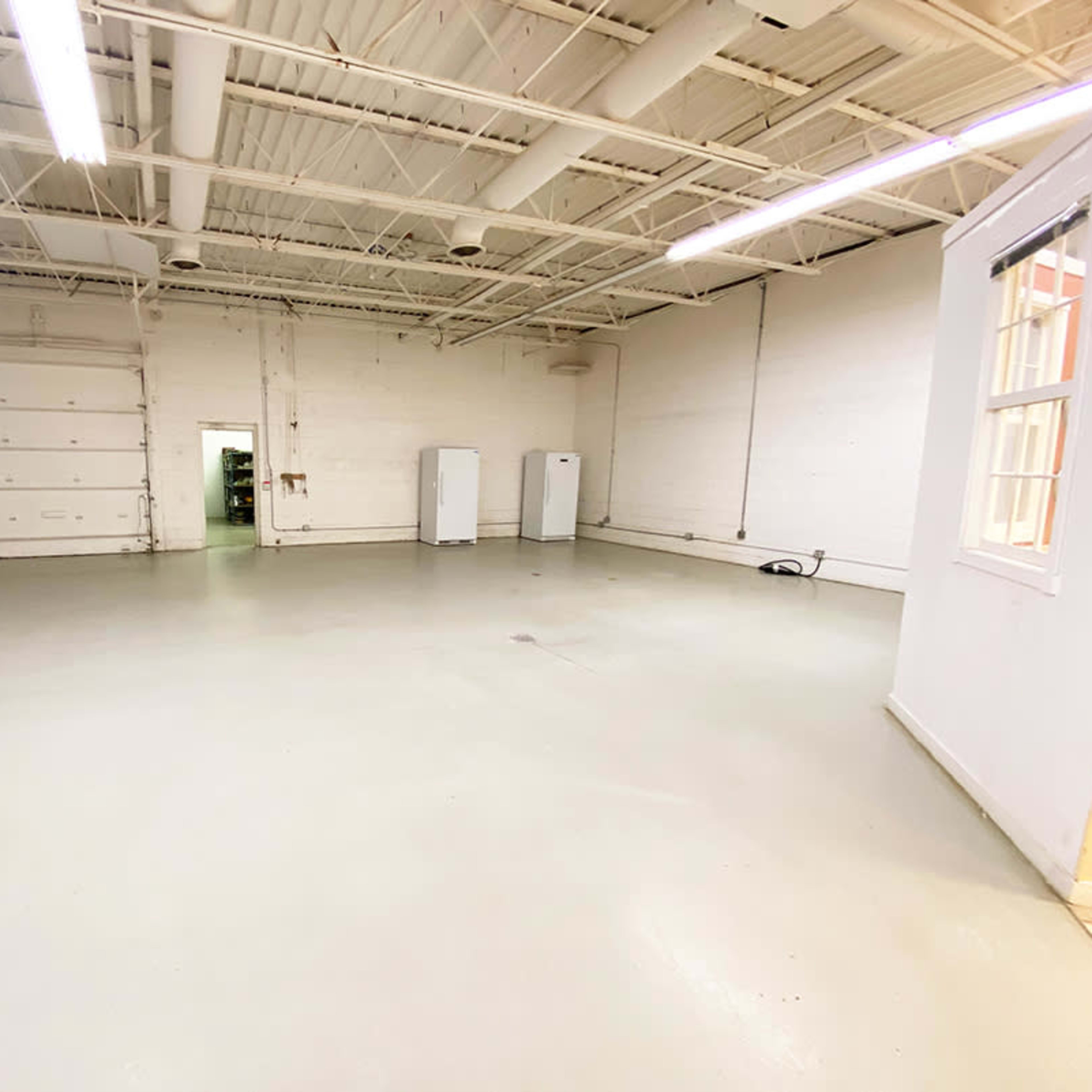 An empty industrial space with a concrete floor, white walls, and several appliances against the walls.