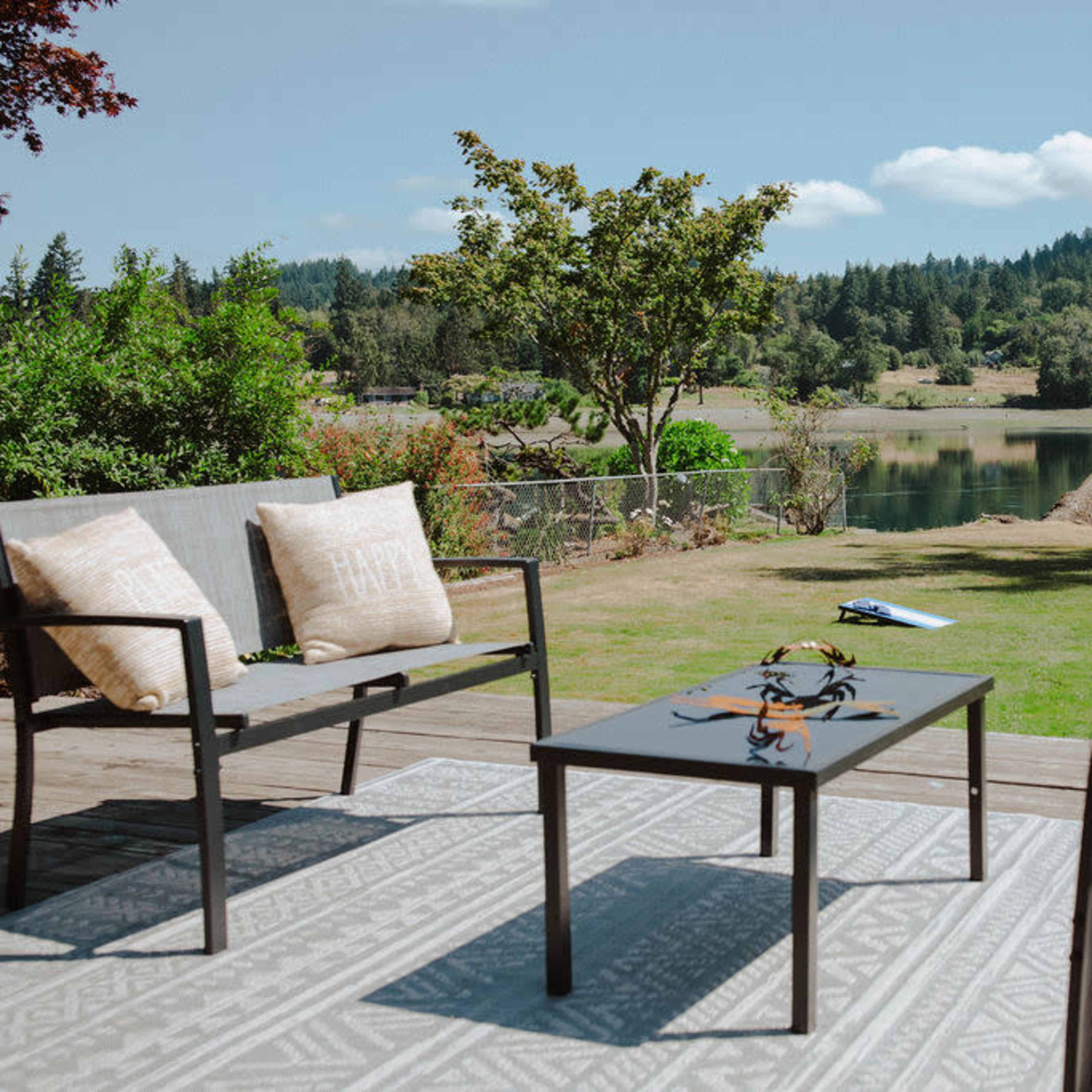 A patio featuring four chairs and a coffee table overlooks a serene lake and green landscape.