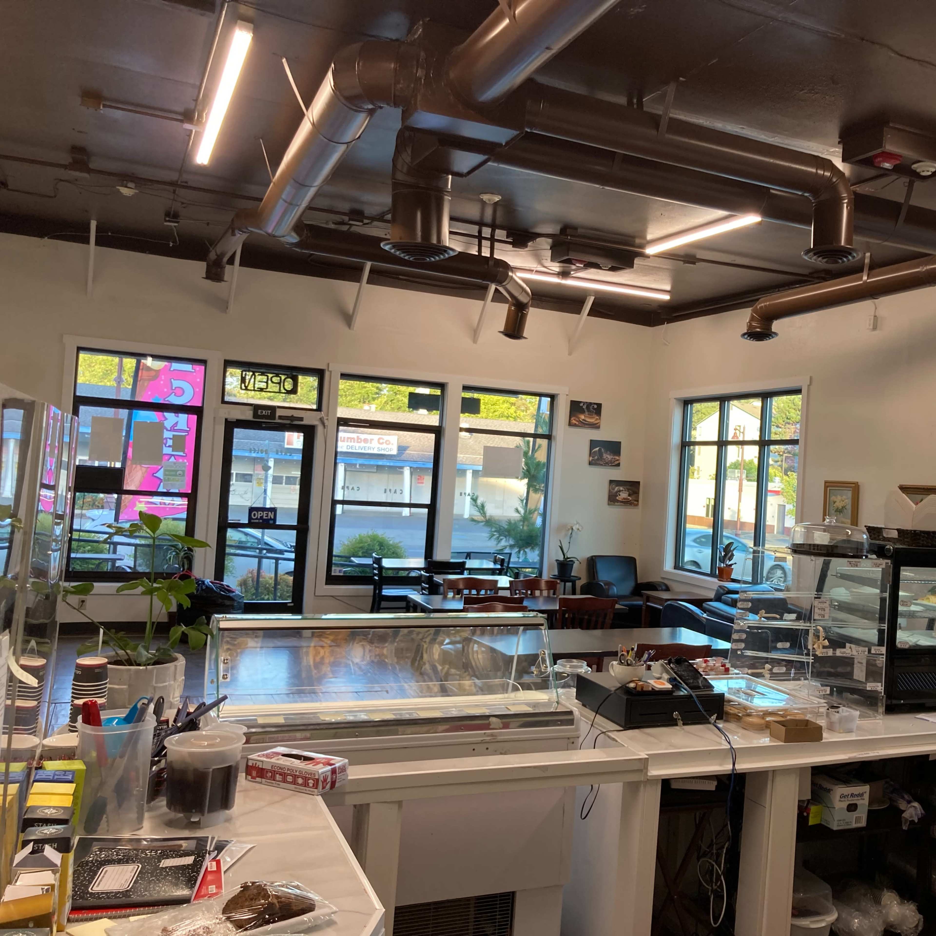 The interior of a café with a counter in the foreground, displaying various items, and large windows offering a view of the street outside.