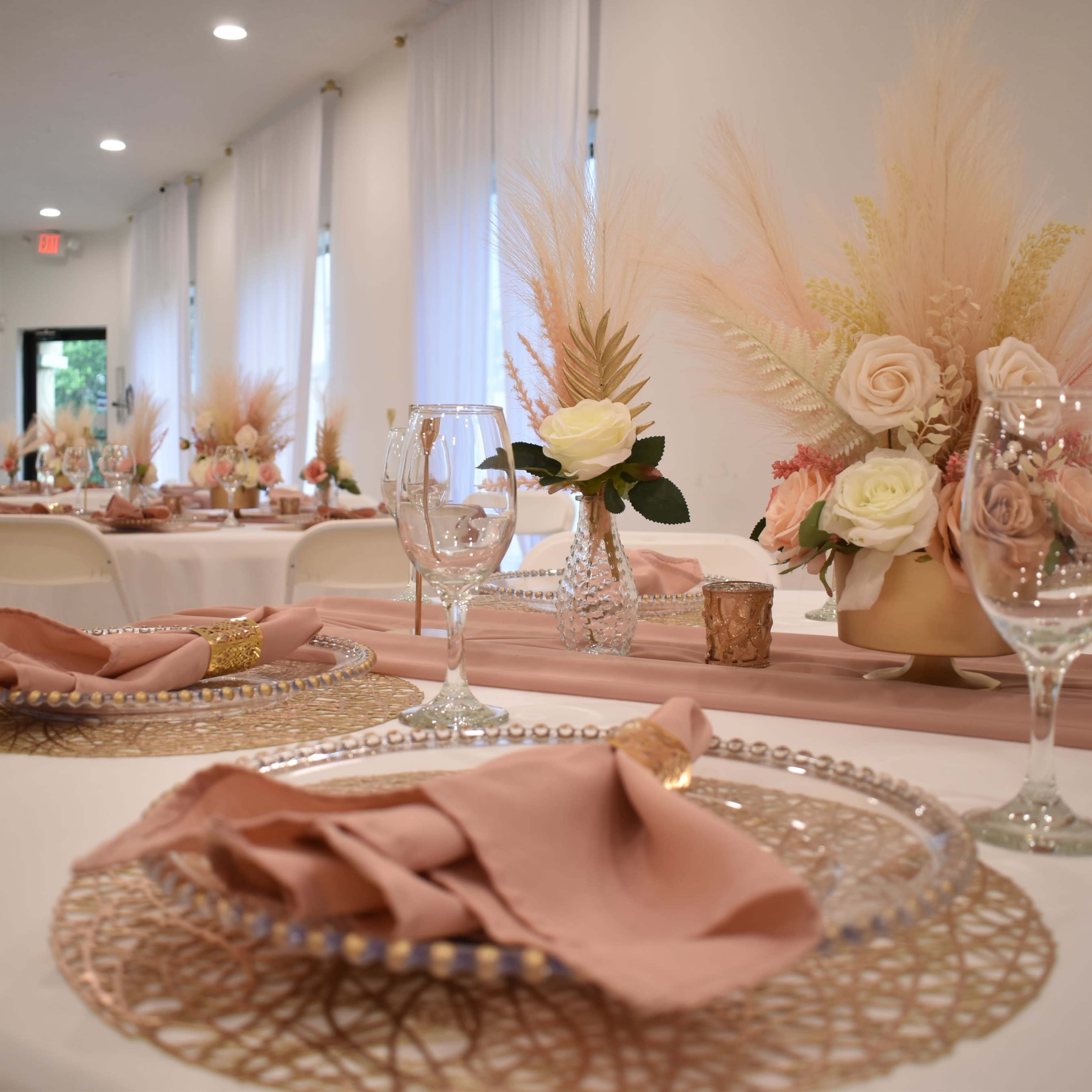 A decorated banquet hall with elegantly set tables featuring floral centerpieces and stylish tableware.