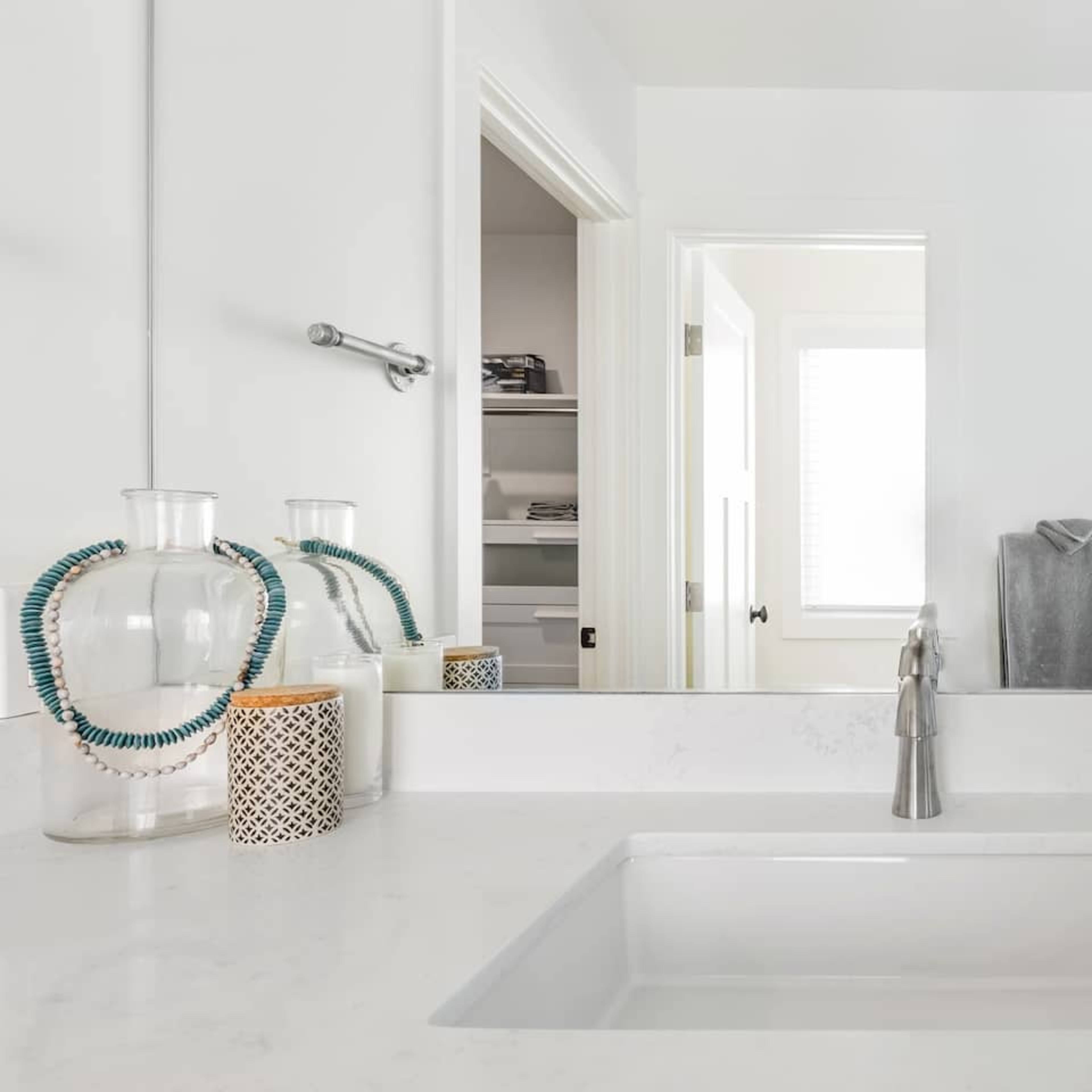 A modern bathroom features a minimalist countertop with a sink, decorative items, and a clear view of an adjoining room through a mirror.