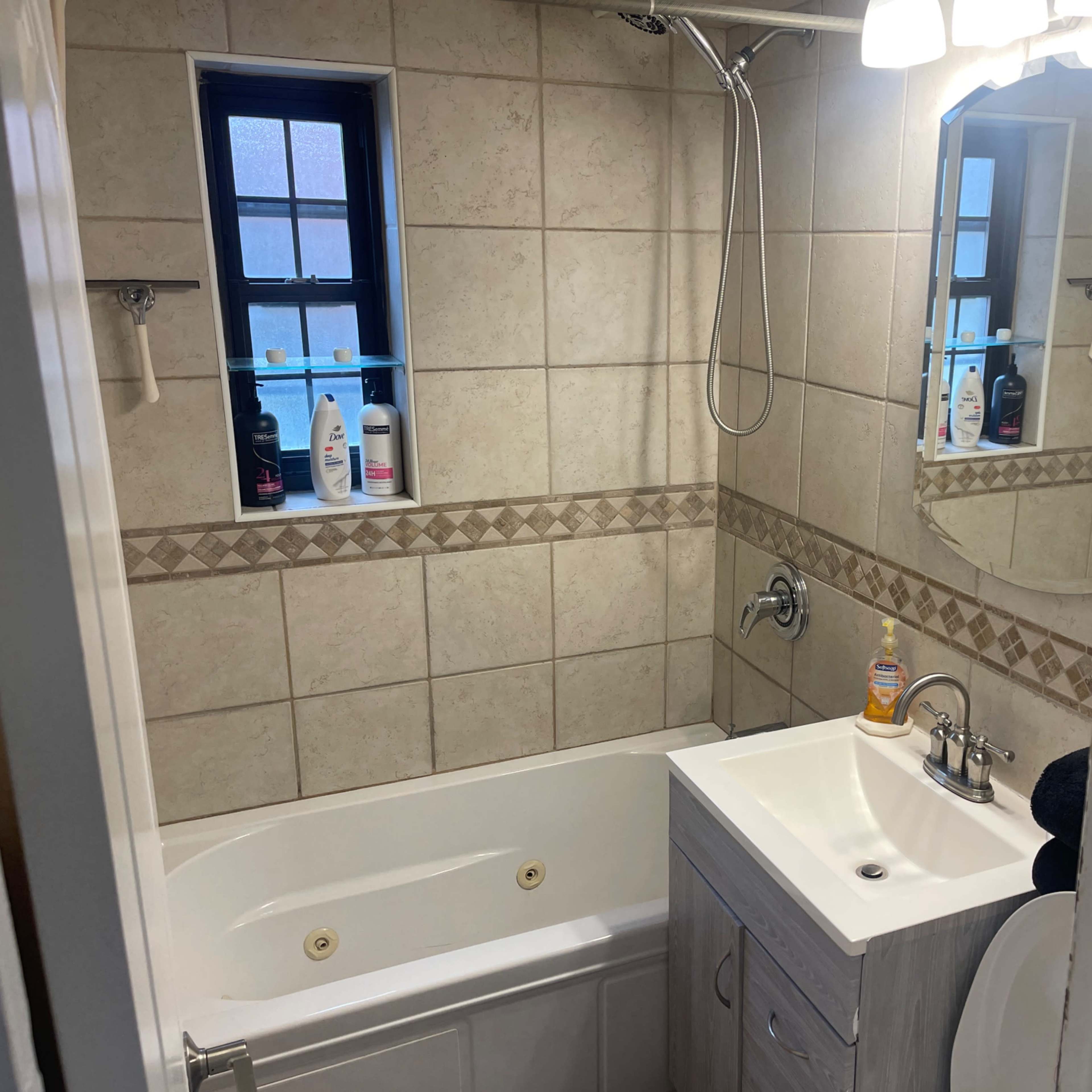 A small bathroom with a bathtub, a sink with a cabinet underneath, and a window above the bathtub.