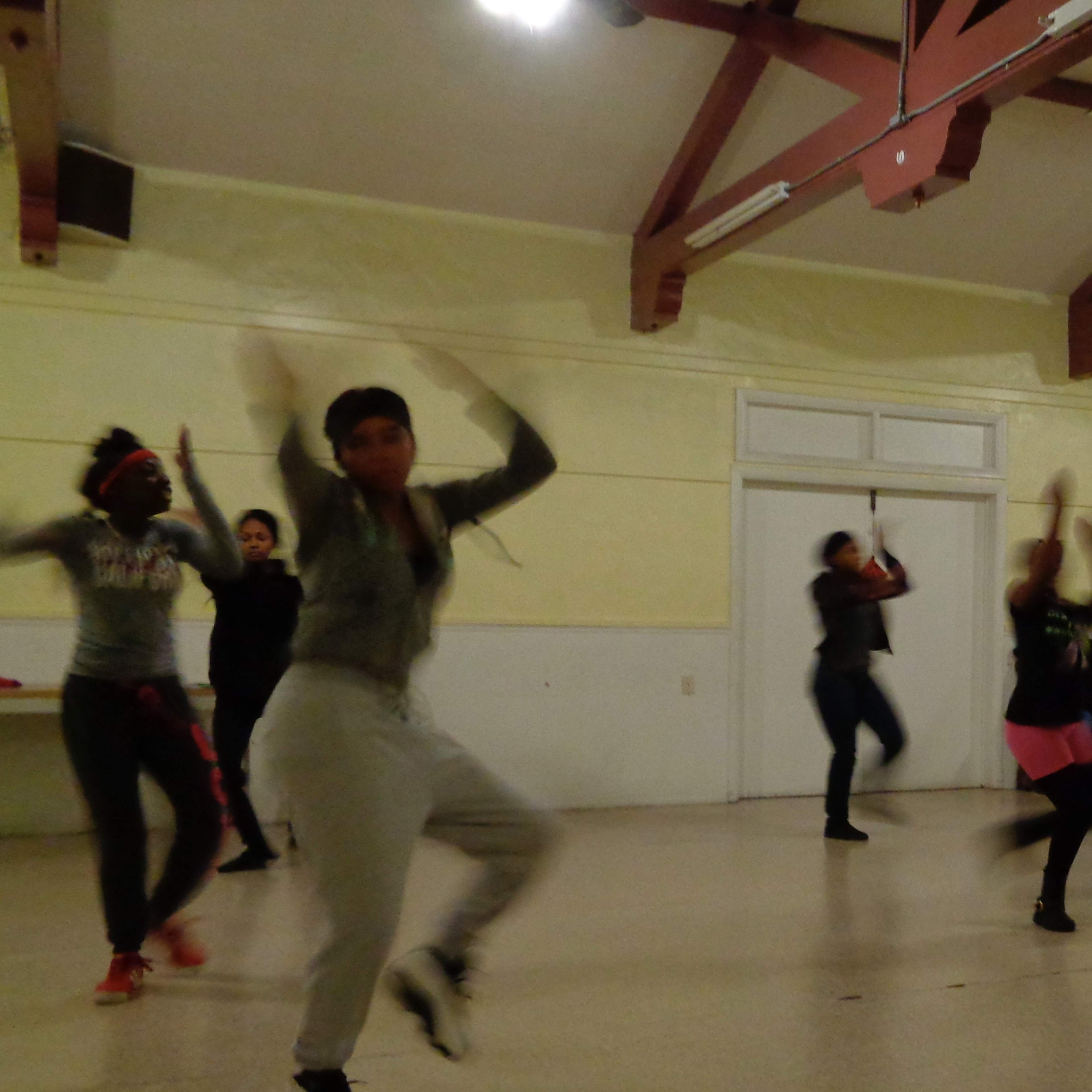 A group of people is dancing in a spacious room with wooden beams and overhead lights.