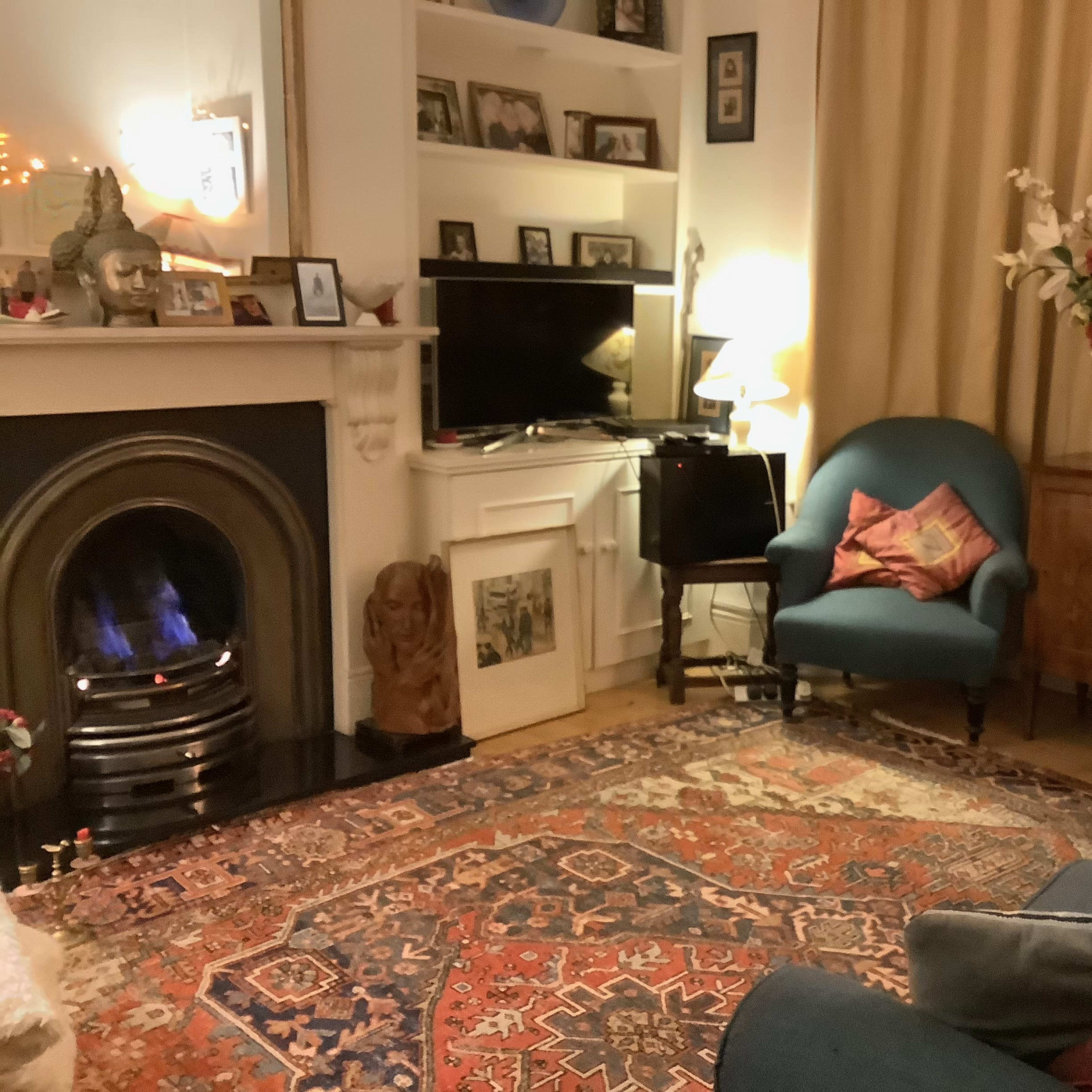 A cozy living room features a blue sofa and armchair, a decorative fireplace with a lion statue, a television, and a floral arrangement on a side table.