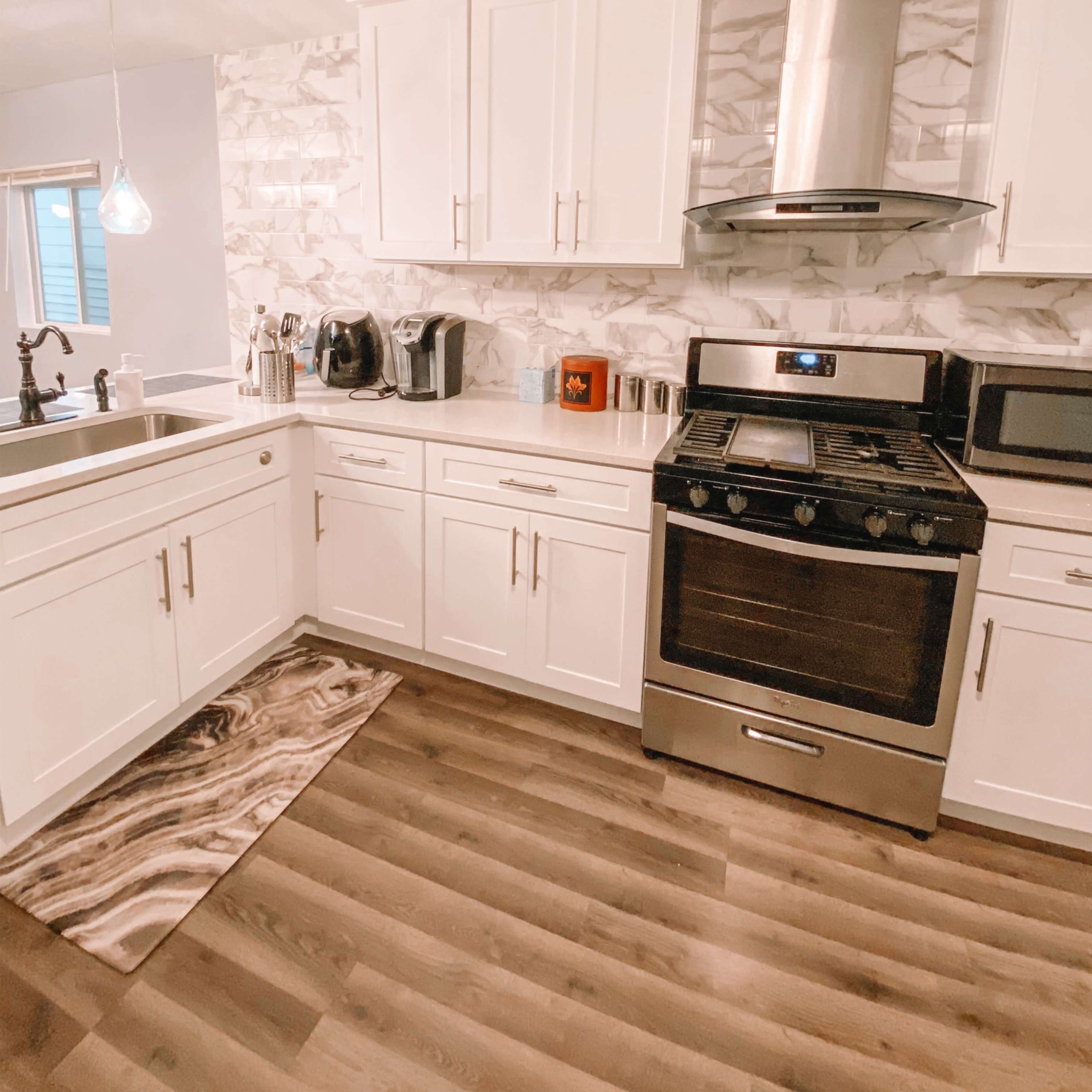 A modern kitchen with white cabinets, a stainless steel stove, and a patterned rug on the wooden floor.