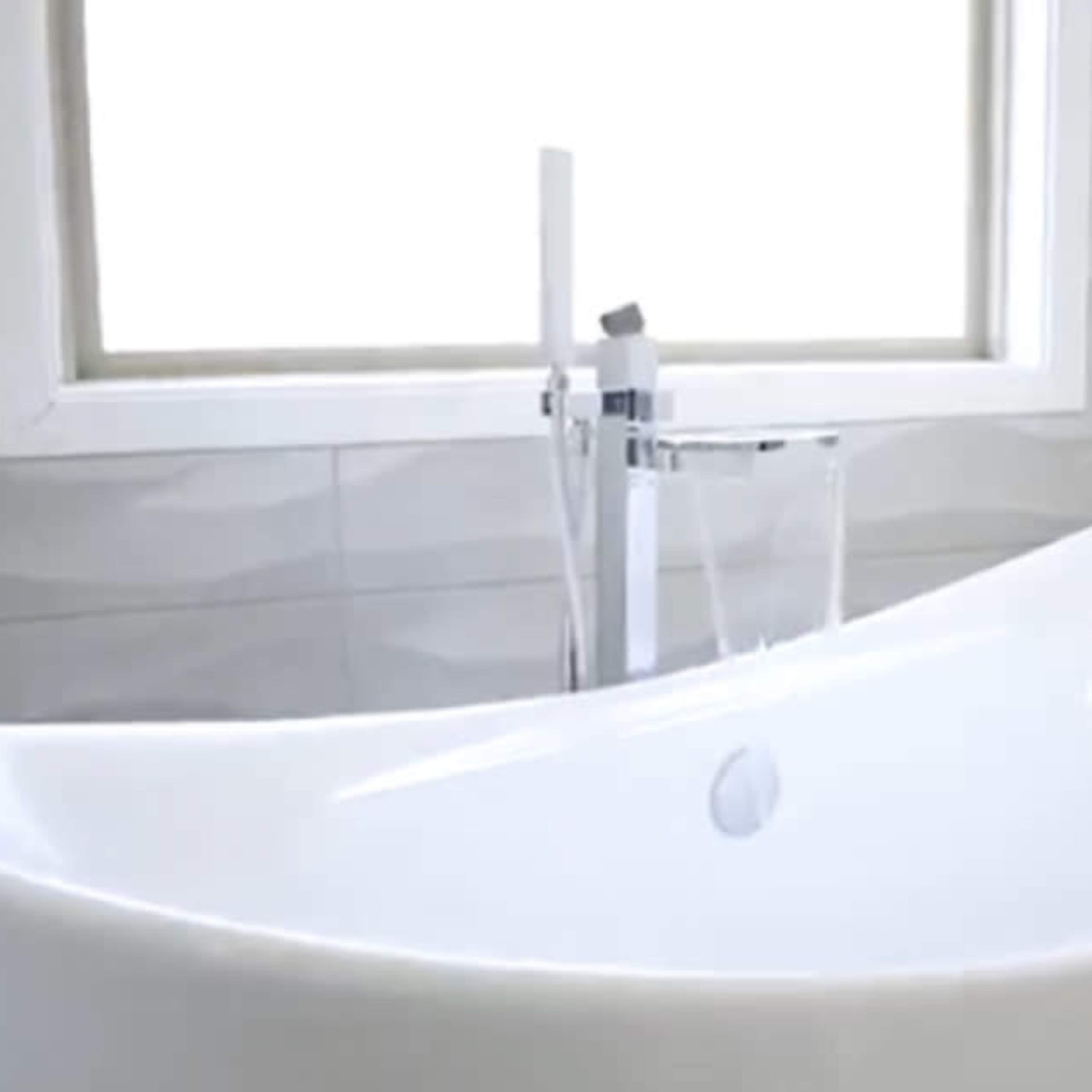 A modern, freestanding white bathtub next to a window in a light-colored bathroom.