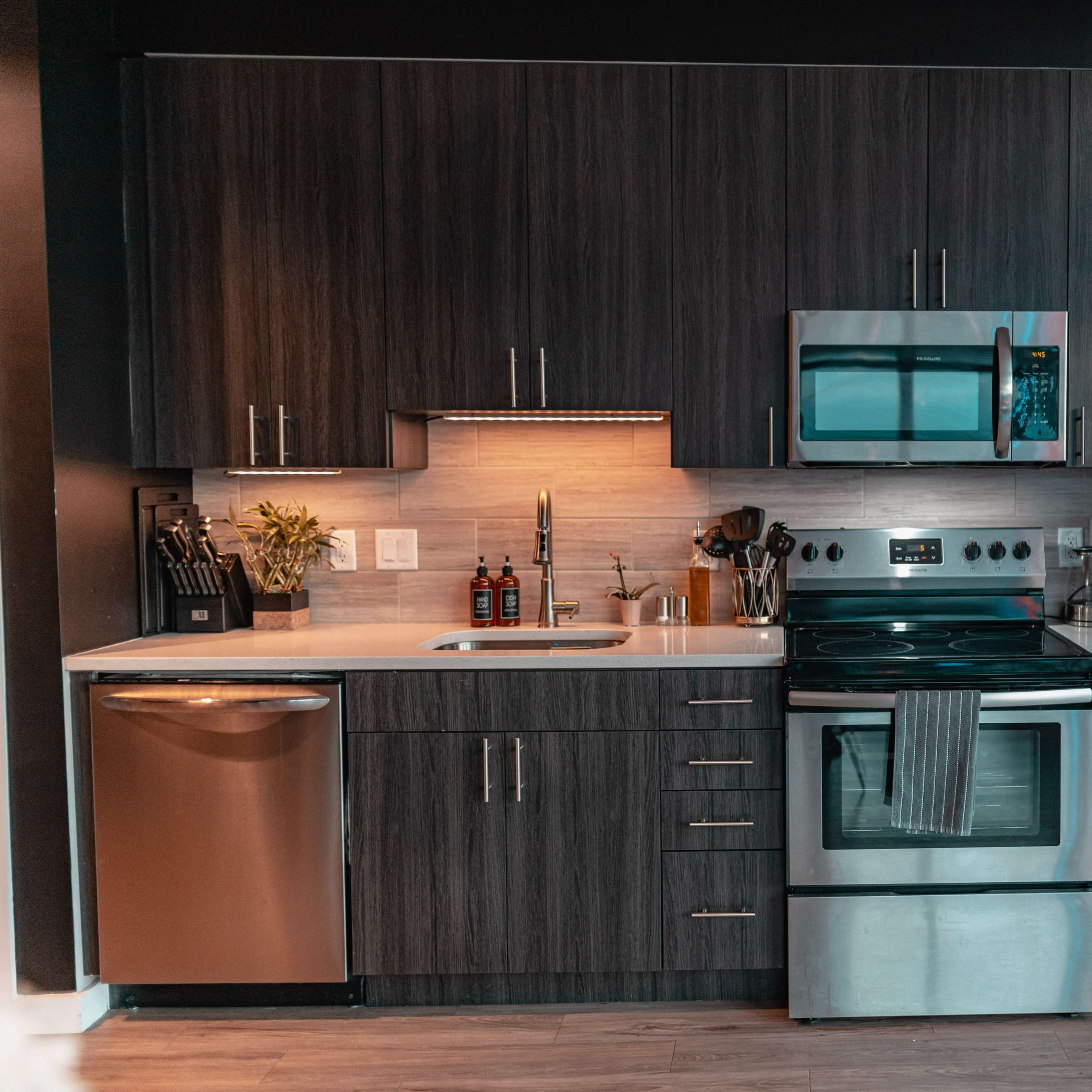 A modern kitchen with dark wood cabinetry, stainless steel appliances, and a countertop with minimalist decor.