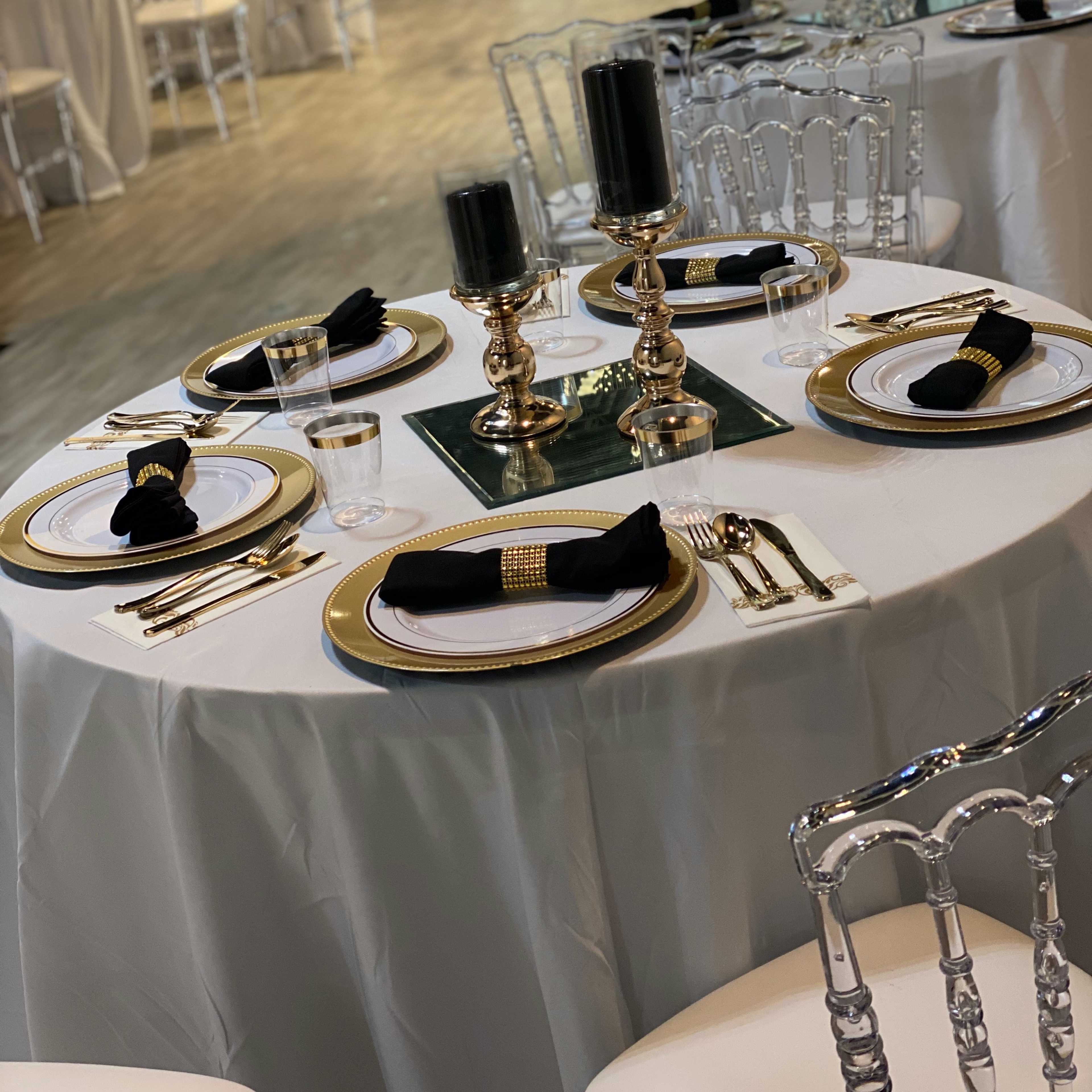 A beautifully arranged dining table with black napkins, elegant silver and gold cutlery, and decorative candlesticks, set in a spacious and light-filled event venue.