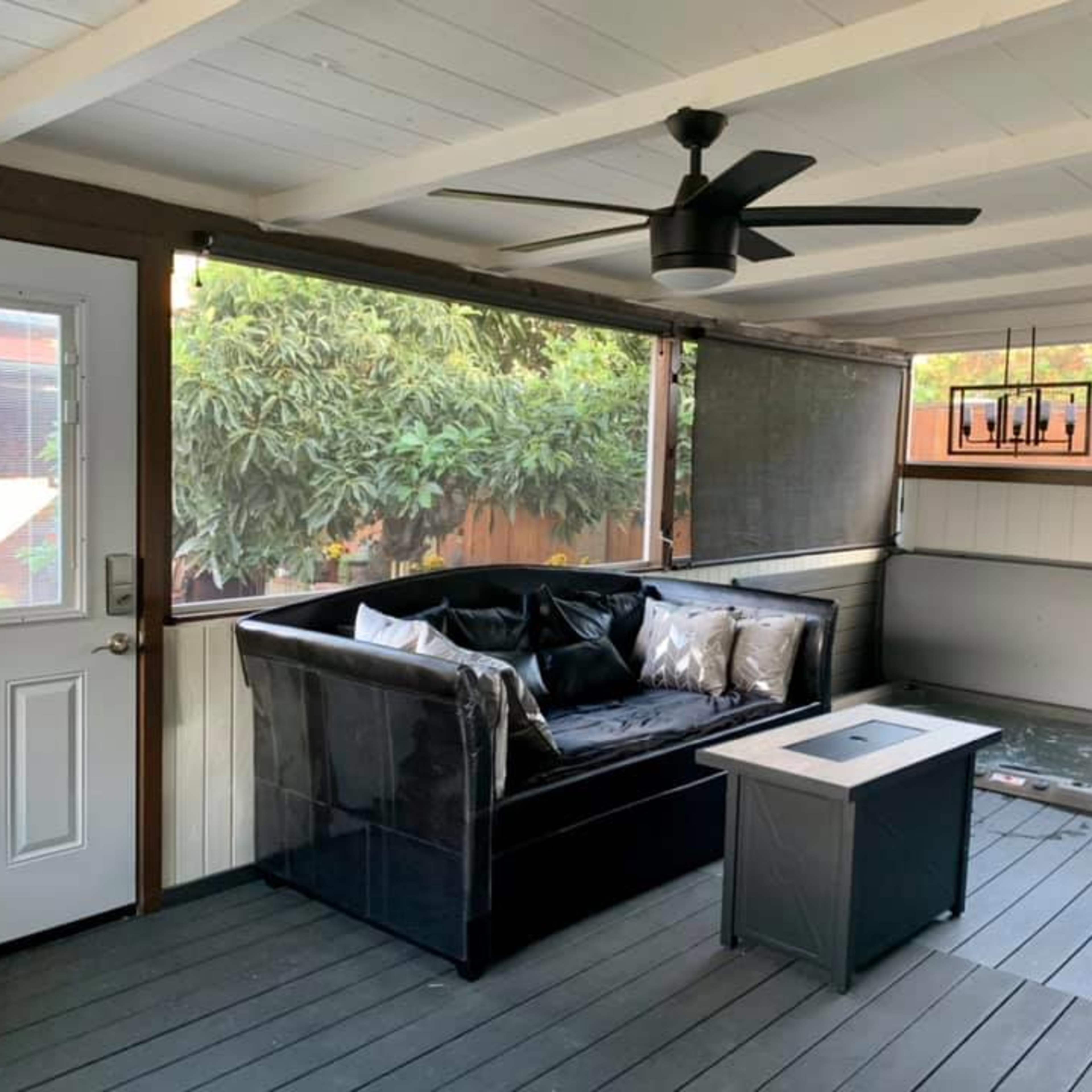 A covered porch area featuring a black couch with cushions, a small table, and a ceiling fan.