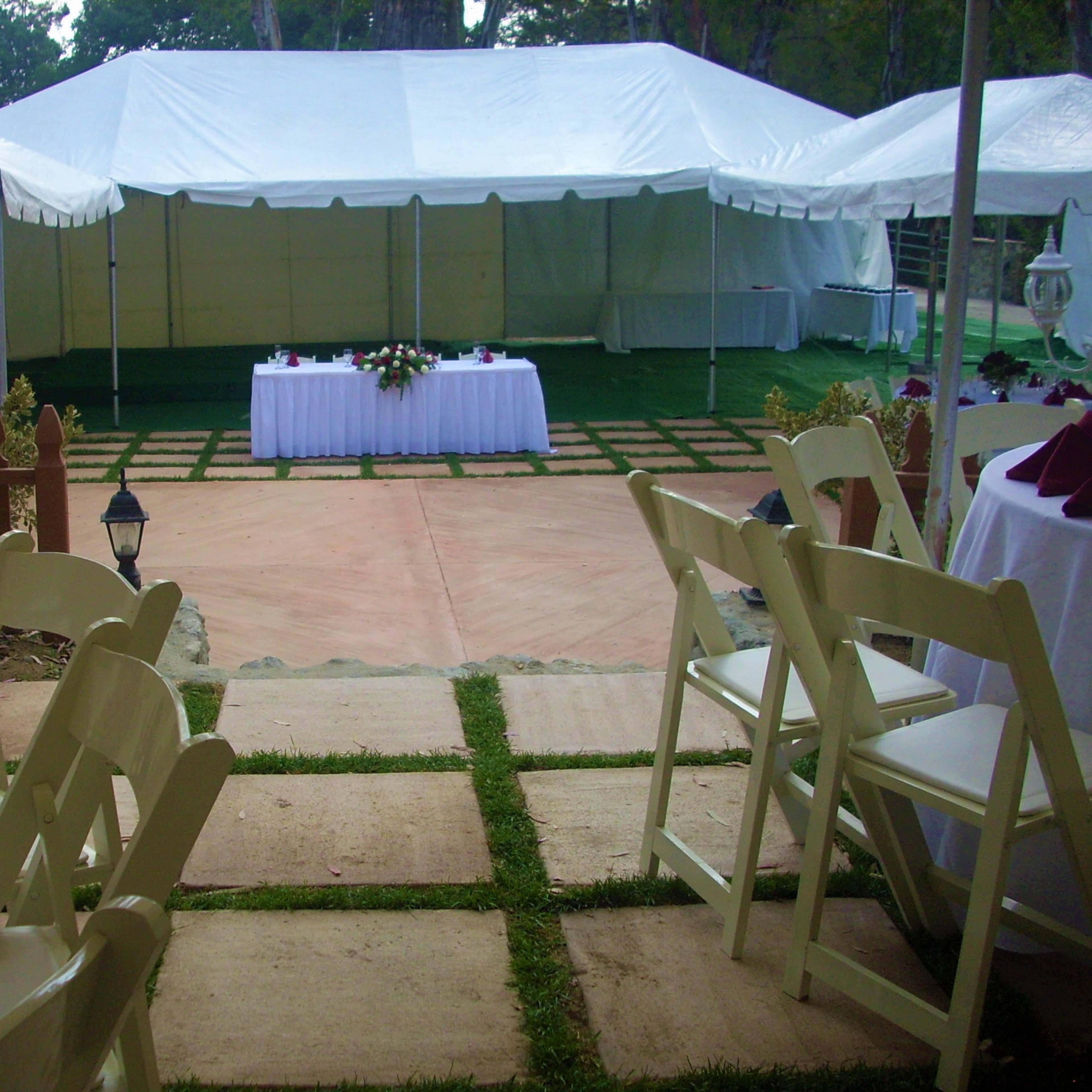 A pathway leading to a large white tent set up for an event, with tables dressed in white and maroon linens in the foreground.