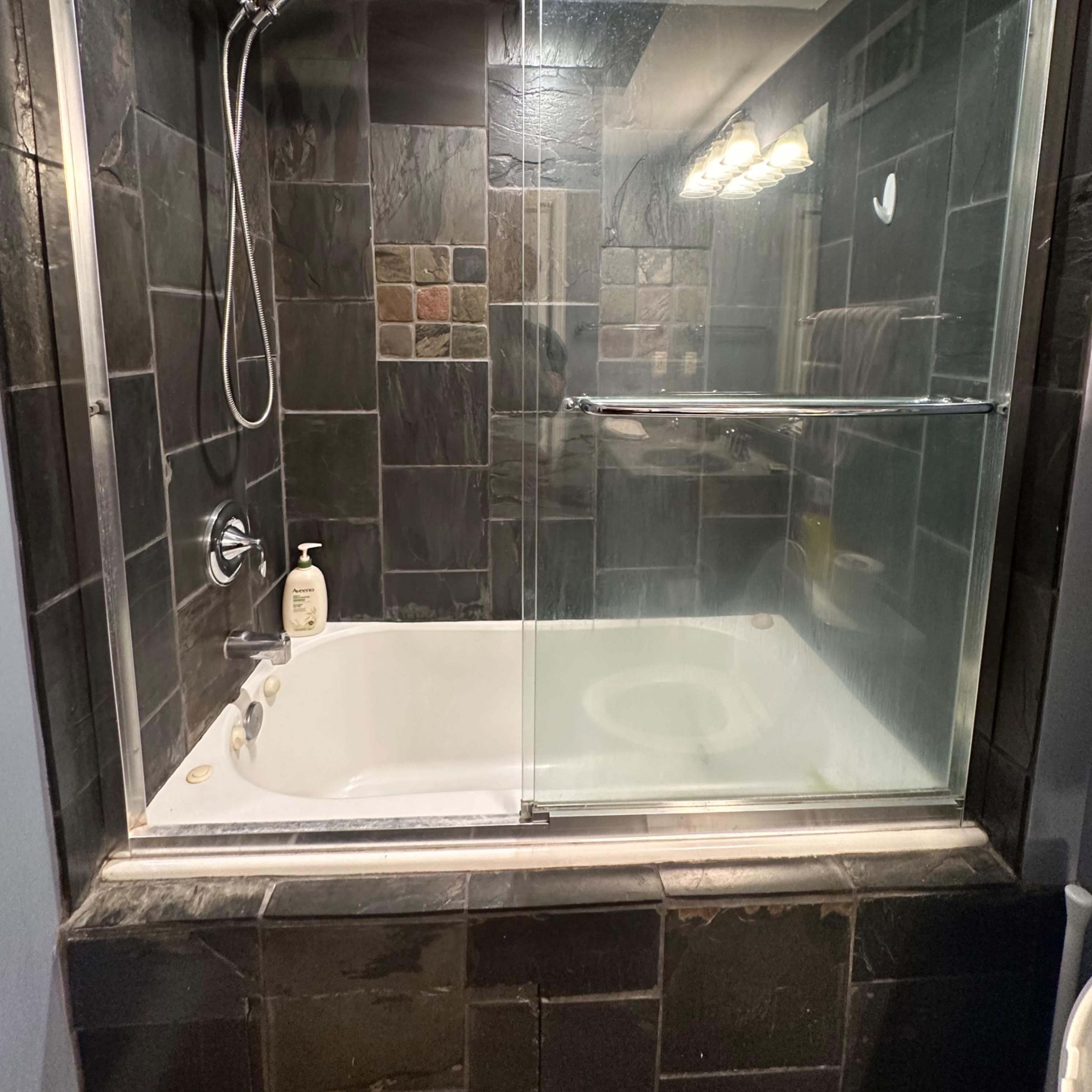 A modern bathroom featuring a glass shower enclosure and a bathtub with a stone tile surround.