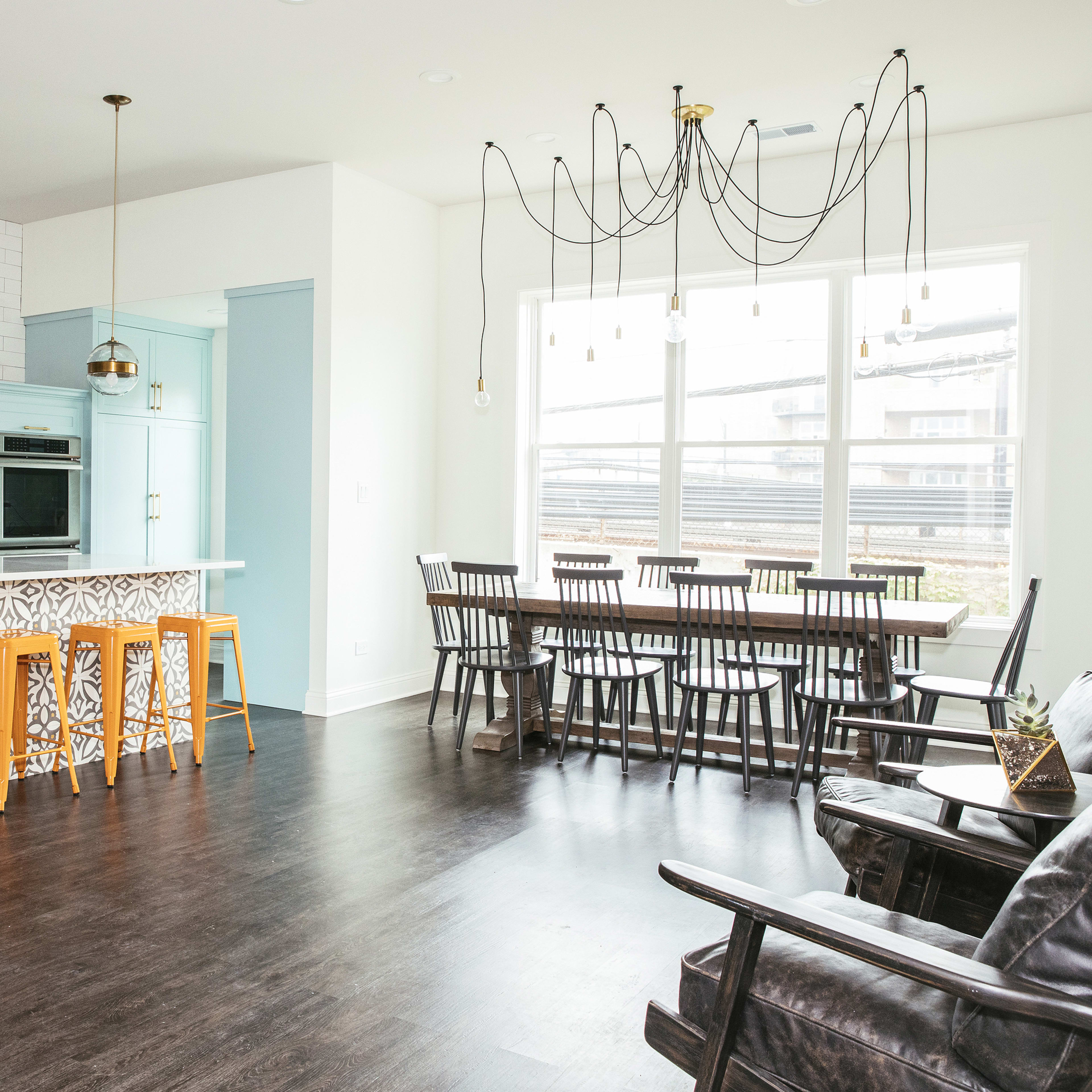 A modern kitchen and dining area with a bar featuring wooden stools, a large dining table, and a stylish light fixture above.