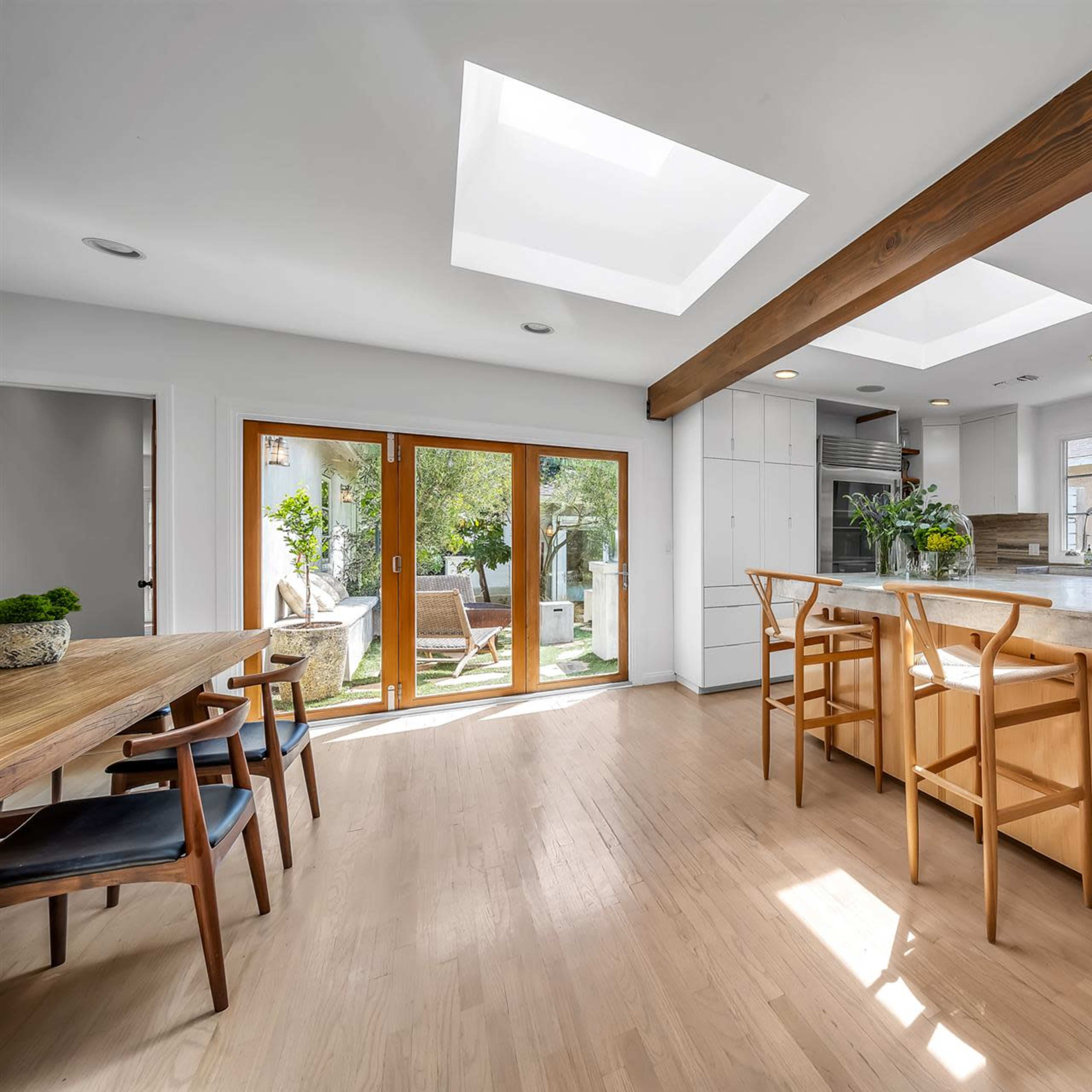 A modern kitchen and dining area featuring a central island, skylights, and large windows opening to a patio.