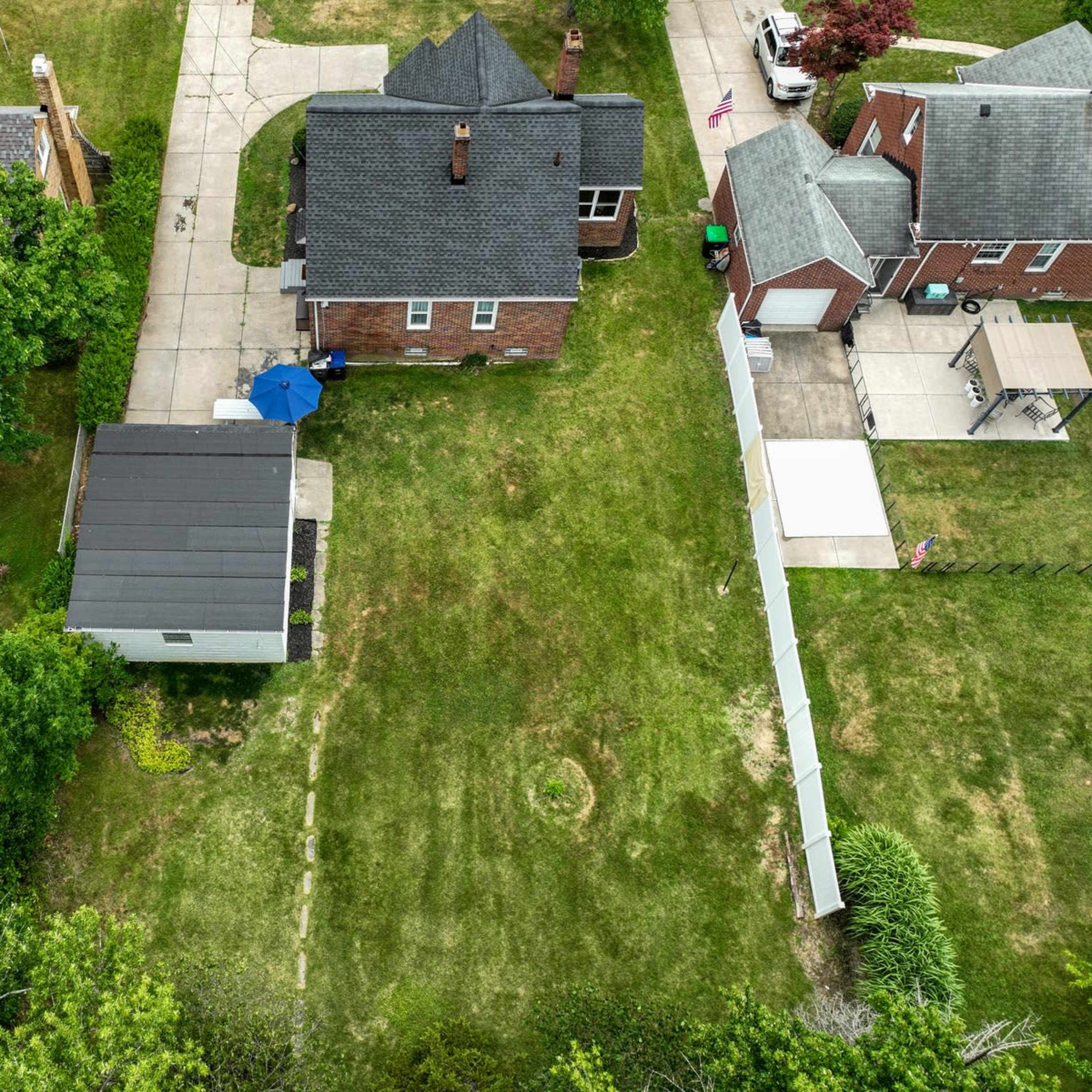 An aerial view of several residential properties with varying roof styles and a backyard featuring a shed and a blue umbrella.