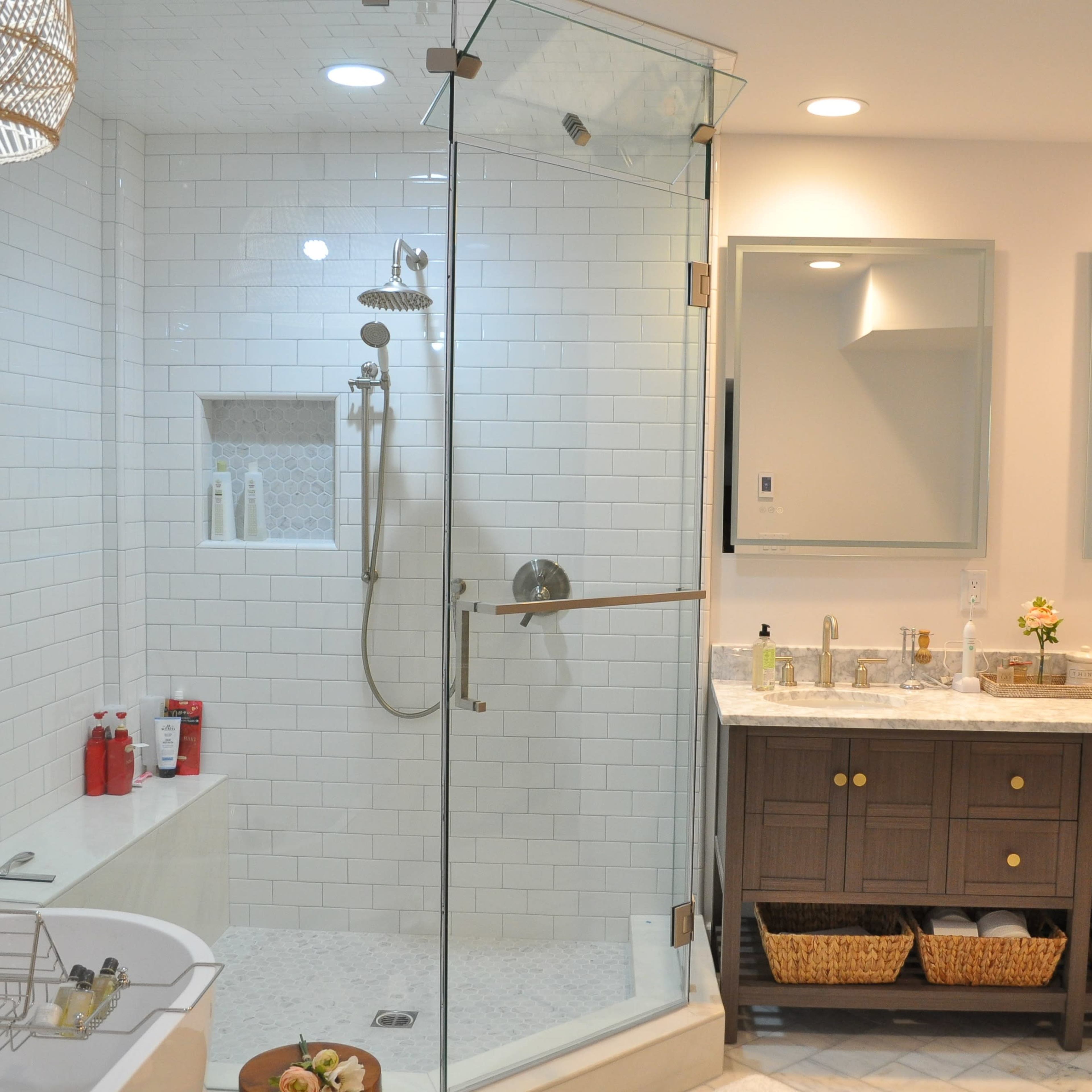 A modern bathroom featuring a glass shower enclosure, a freestanding tub, dual sinks with a marble countertop, and wooden cabinetry.