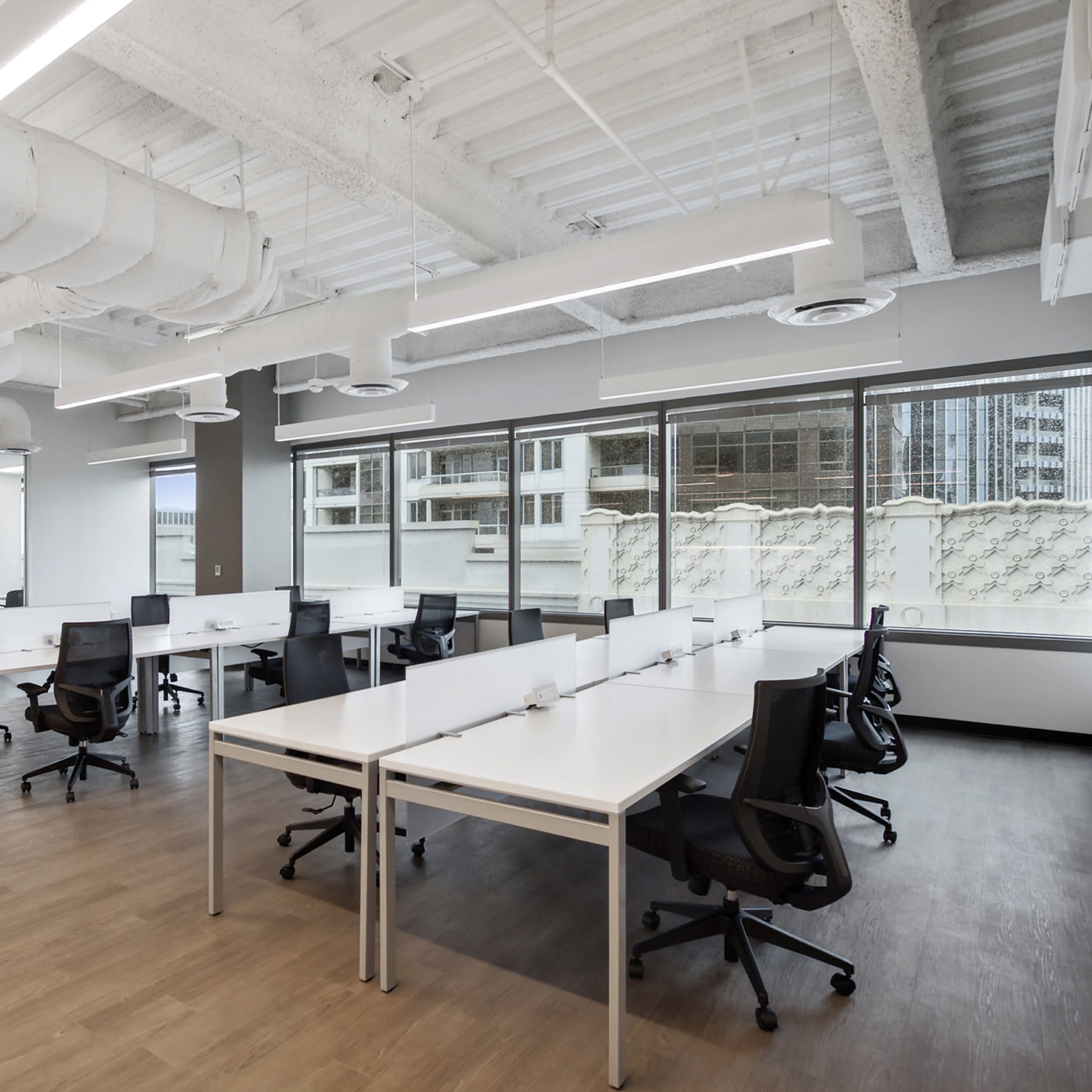 A modern office space featuring several white desks and black chairs arranged in an open layout with large windows.