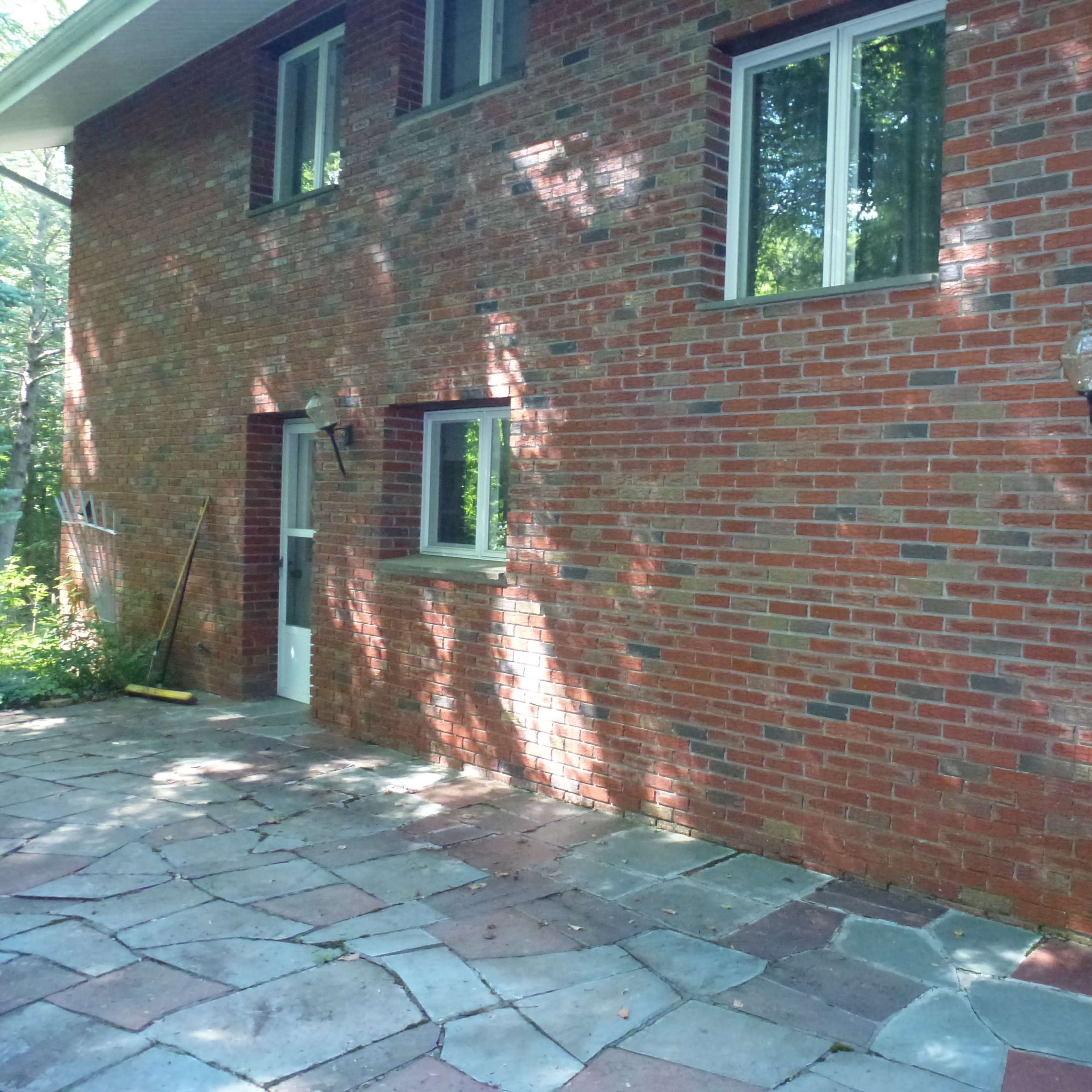 A section of a brick house with several windows and a stone patio.