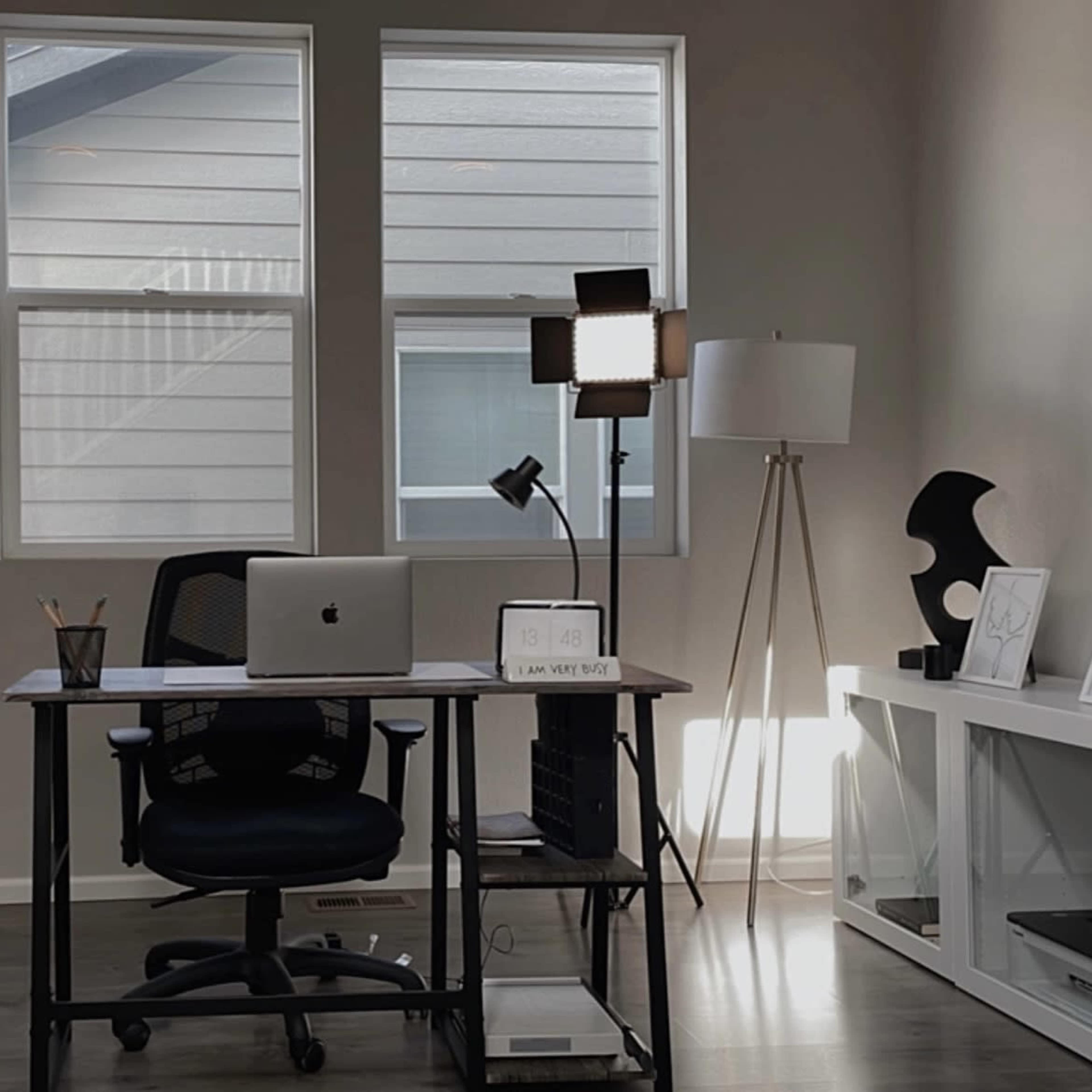 A modern office space with a black desk, an open laptop, two floor lamps, and decorative items on a shelf.