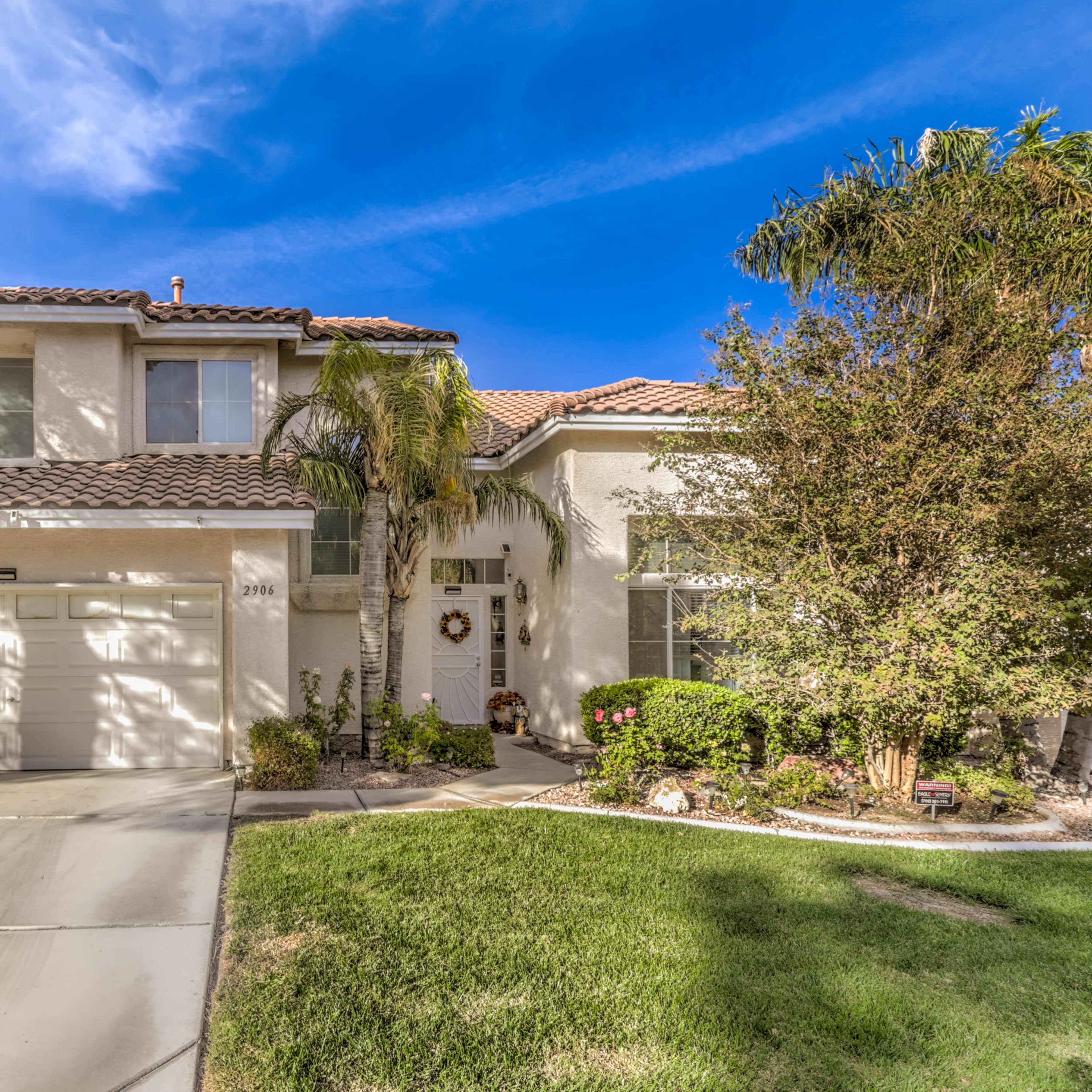 A two-story house with a tile roof, palm trees, and a well-maintained front yard.