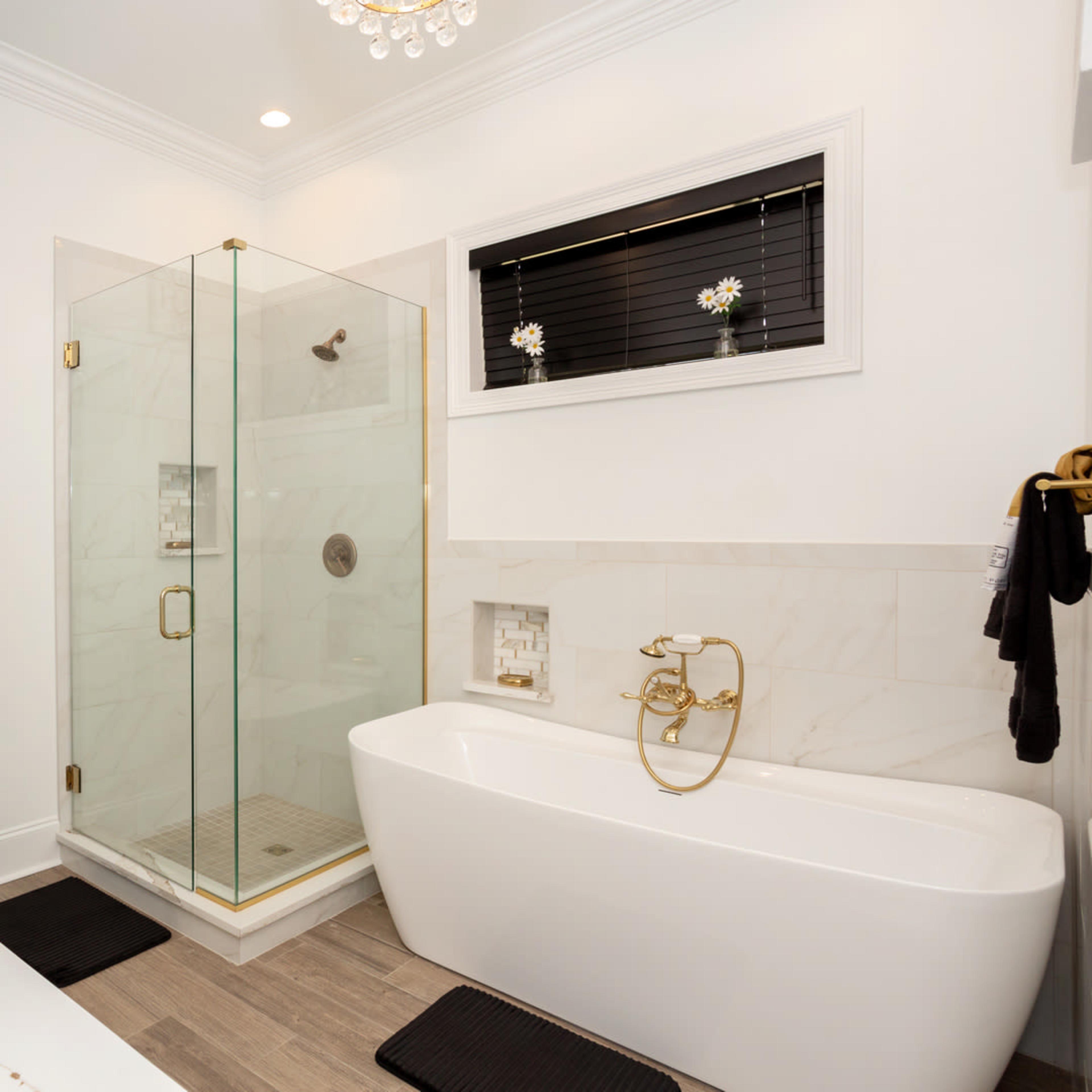 A modern bathroom featuring a glass shower enclosure, a freestanding tub, dual sinks with vessel faucets, and elegant gold hardware.