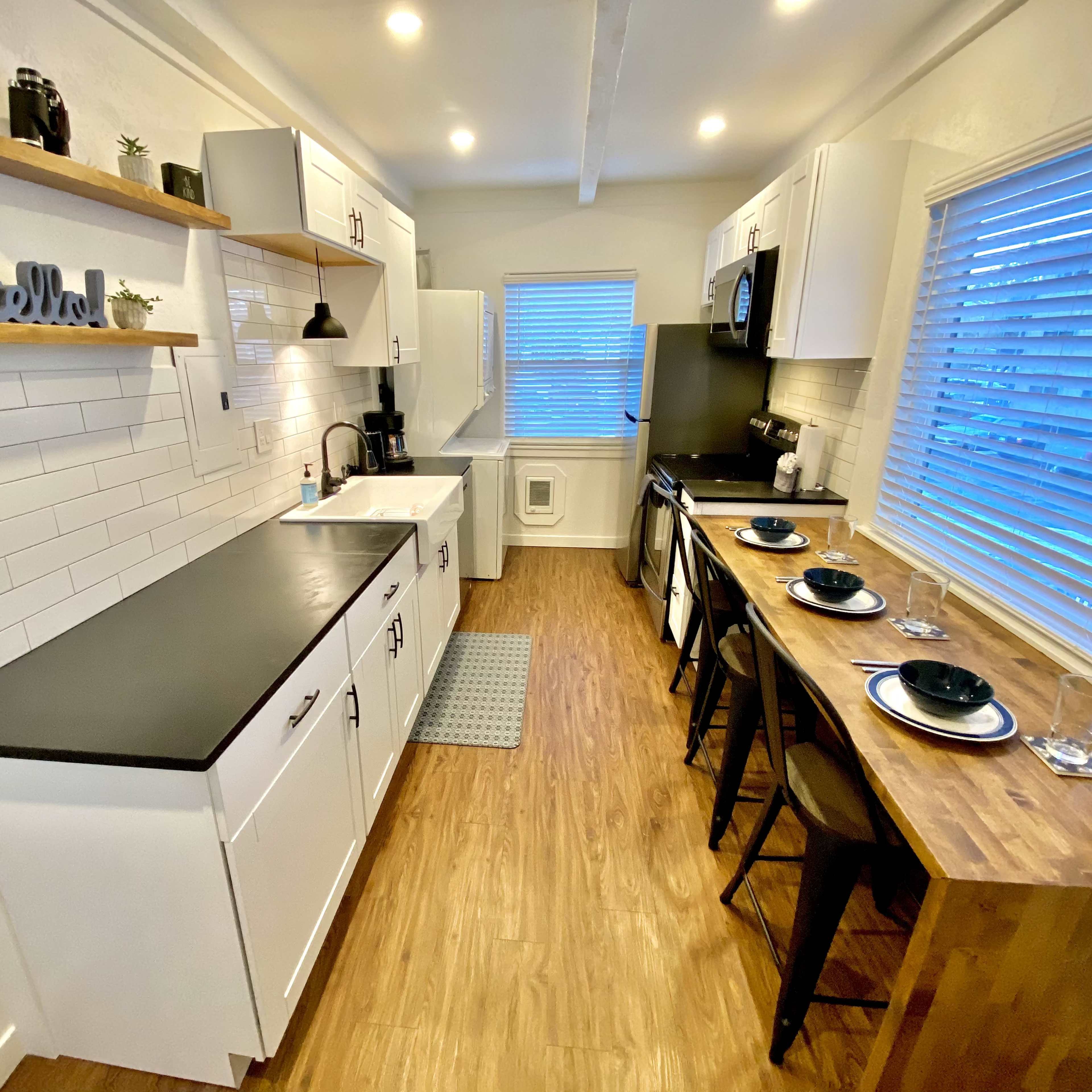 A modern kitchen with white cabinets, a black countertop, and a dining area with wooden seating.