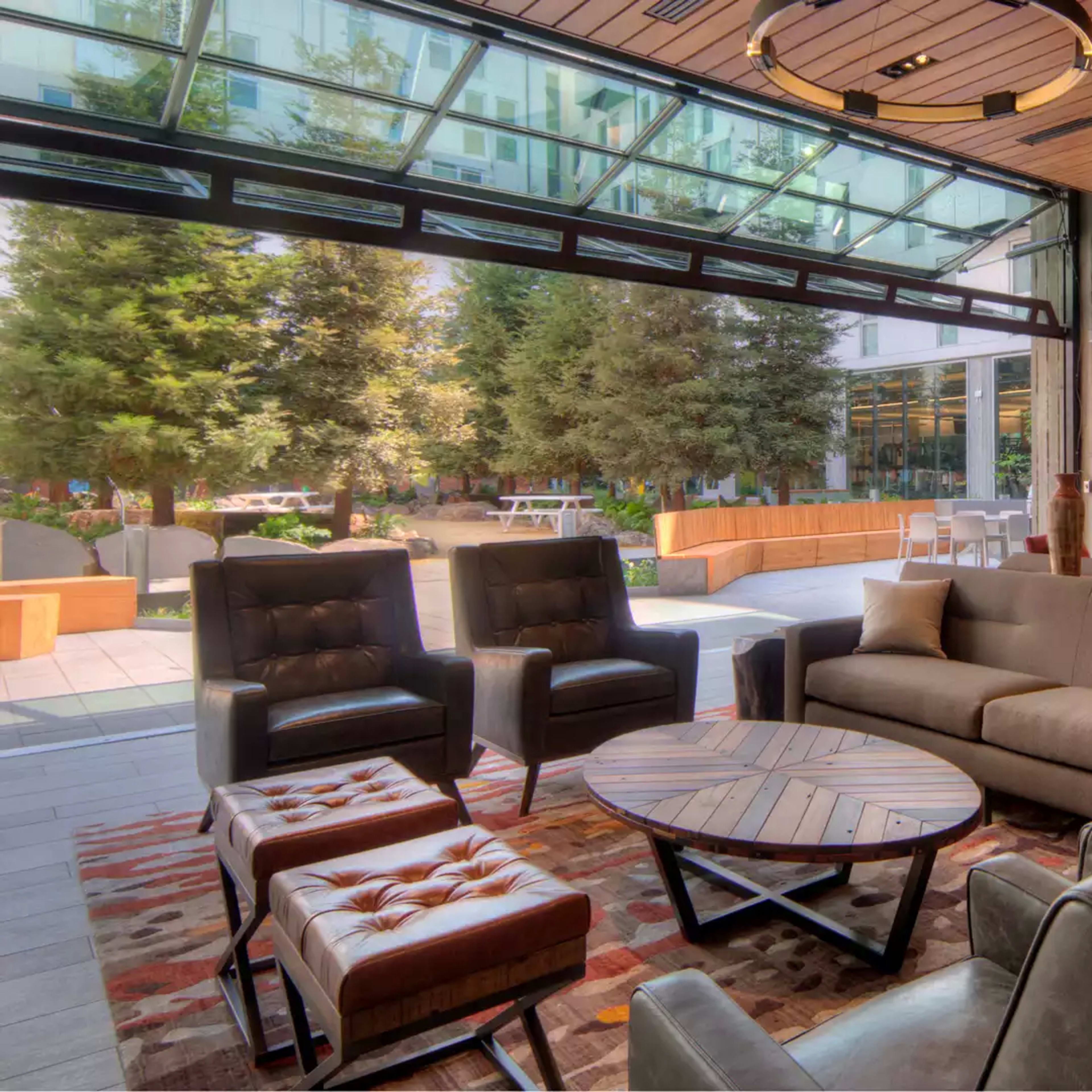 A modern lounge area with a mix of seating options, large windows opening to an outdoor space, and wooden accents on the walls.