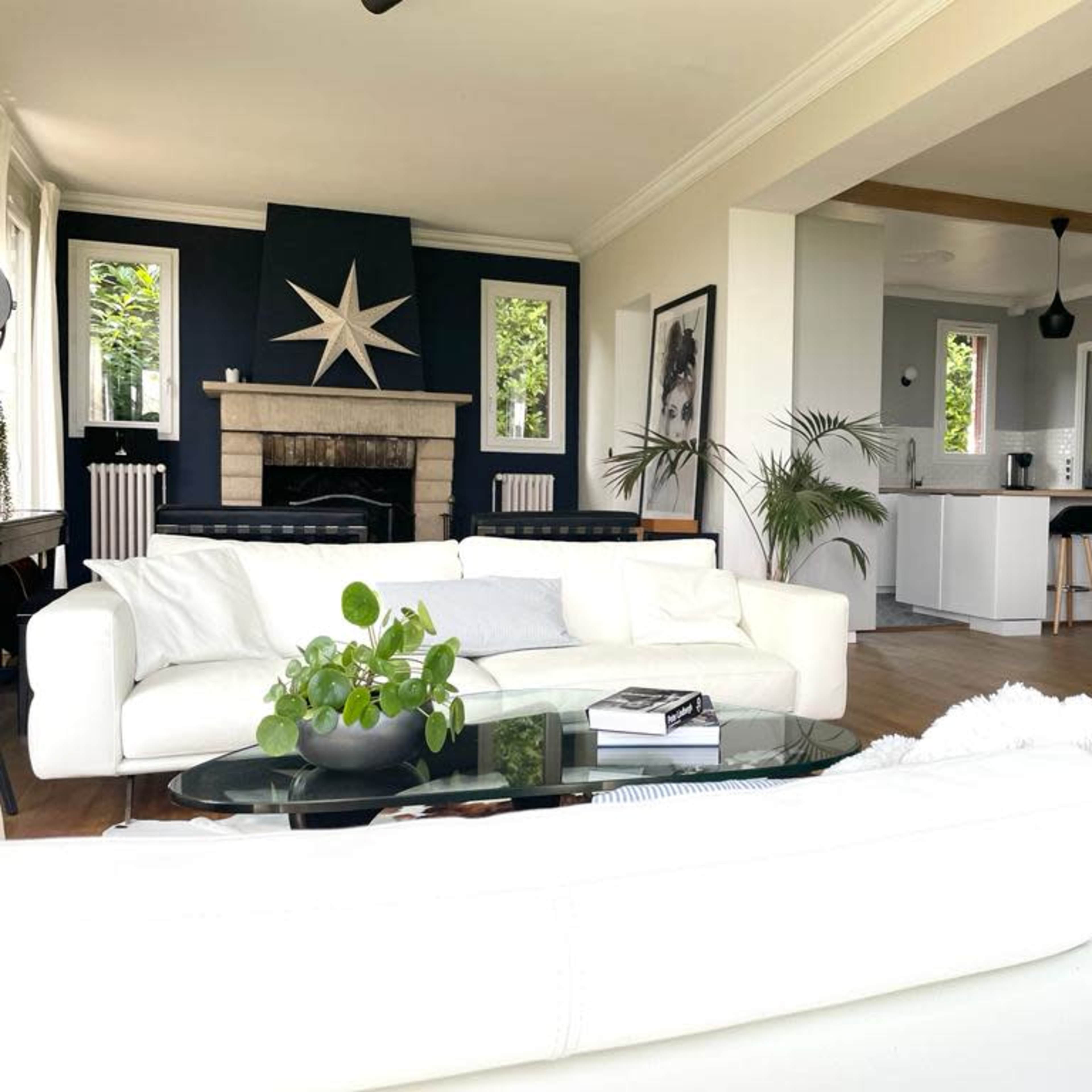 A modern living room features a white sectional sofa, a glass coffee table with a plant, and a stylish fireplace, leading to an open kitchen with a minimalist design.