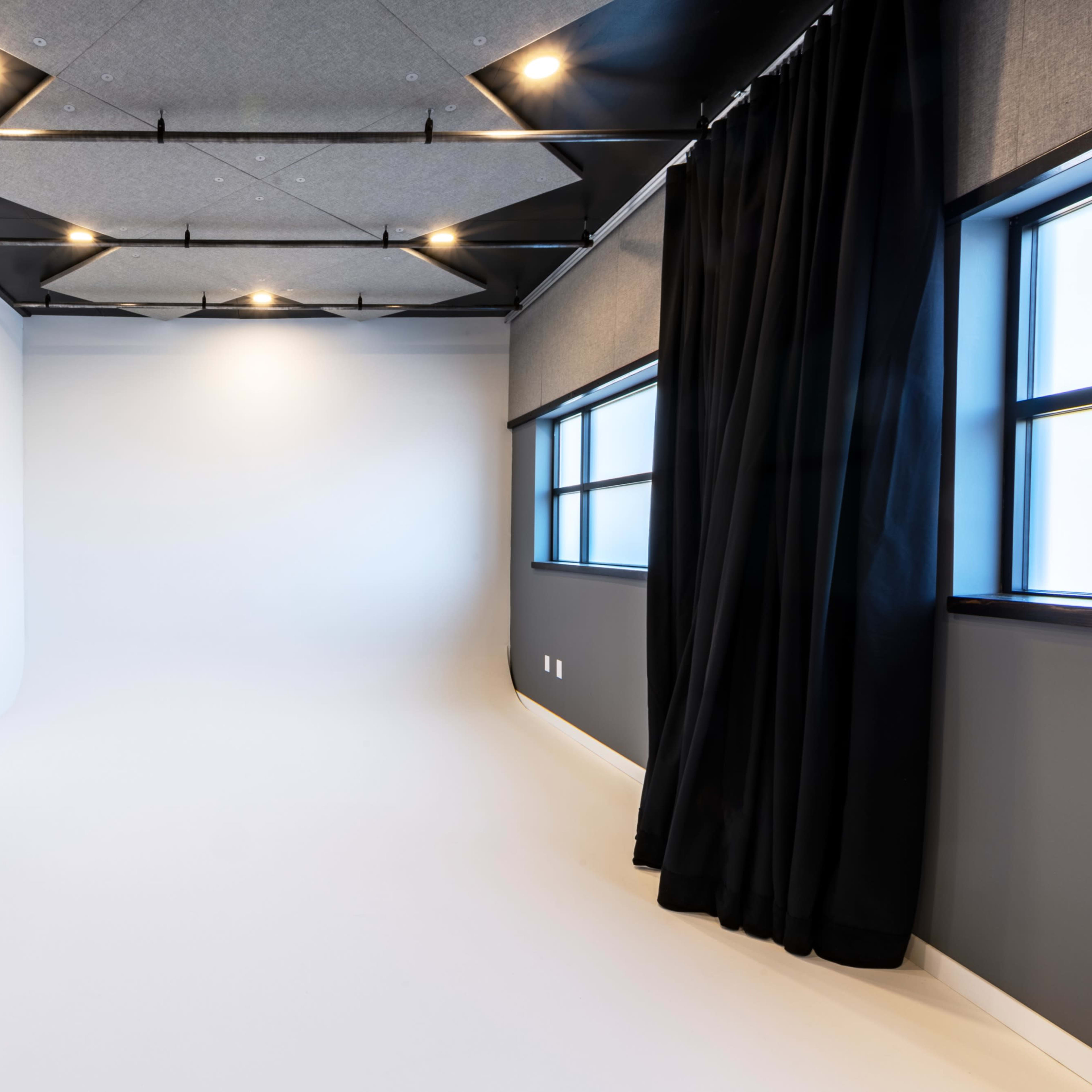 A minimalist studio space with white walls, large windows, and a black curtain in one corner.