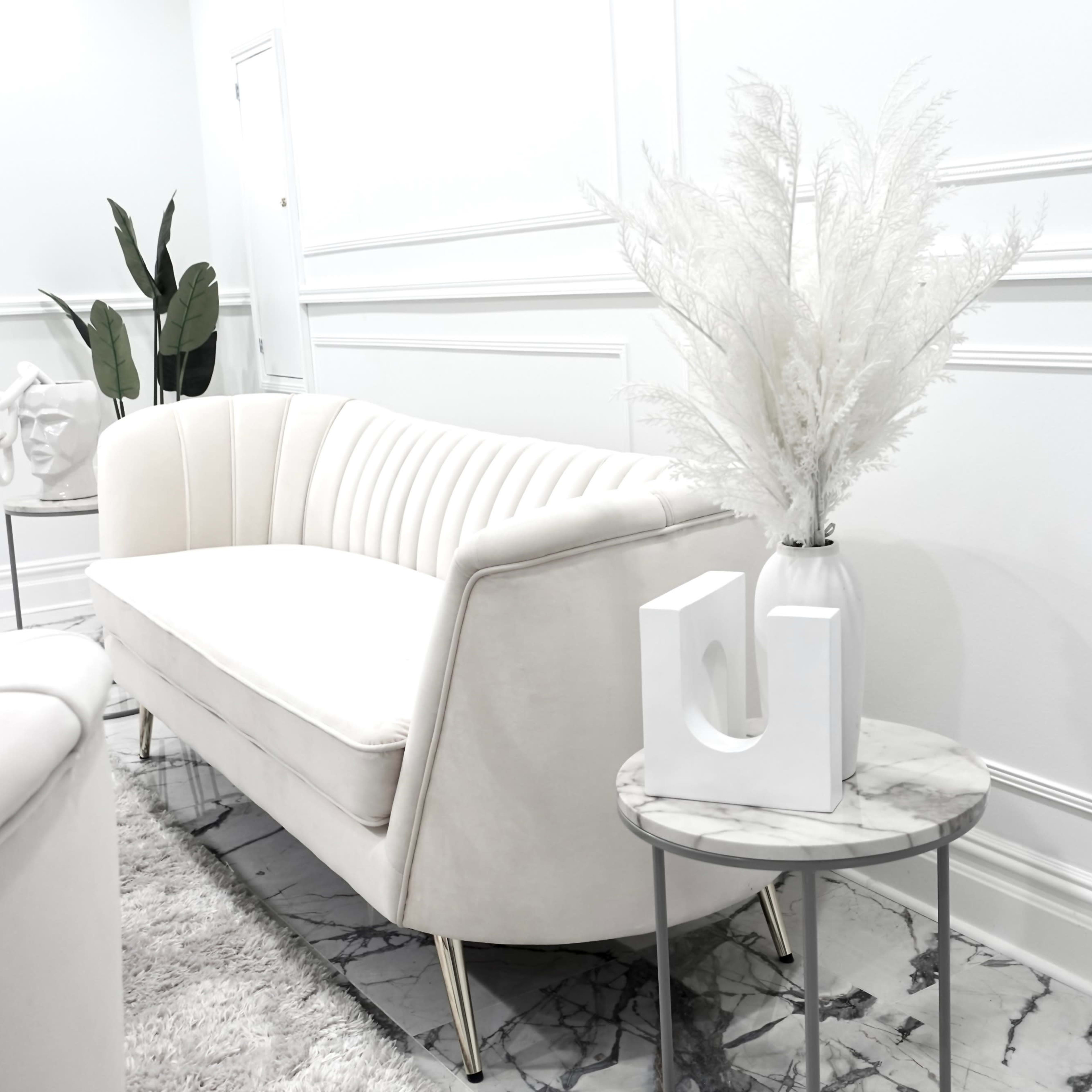 A white upholstered sofa is positioned next to a small marble-topped side table holding a minimalist white vase with decorative foliage.