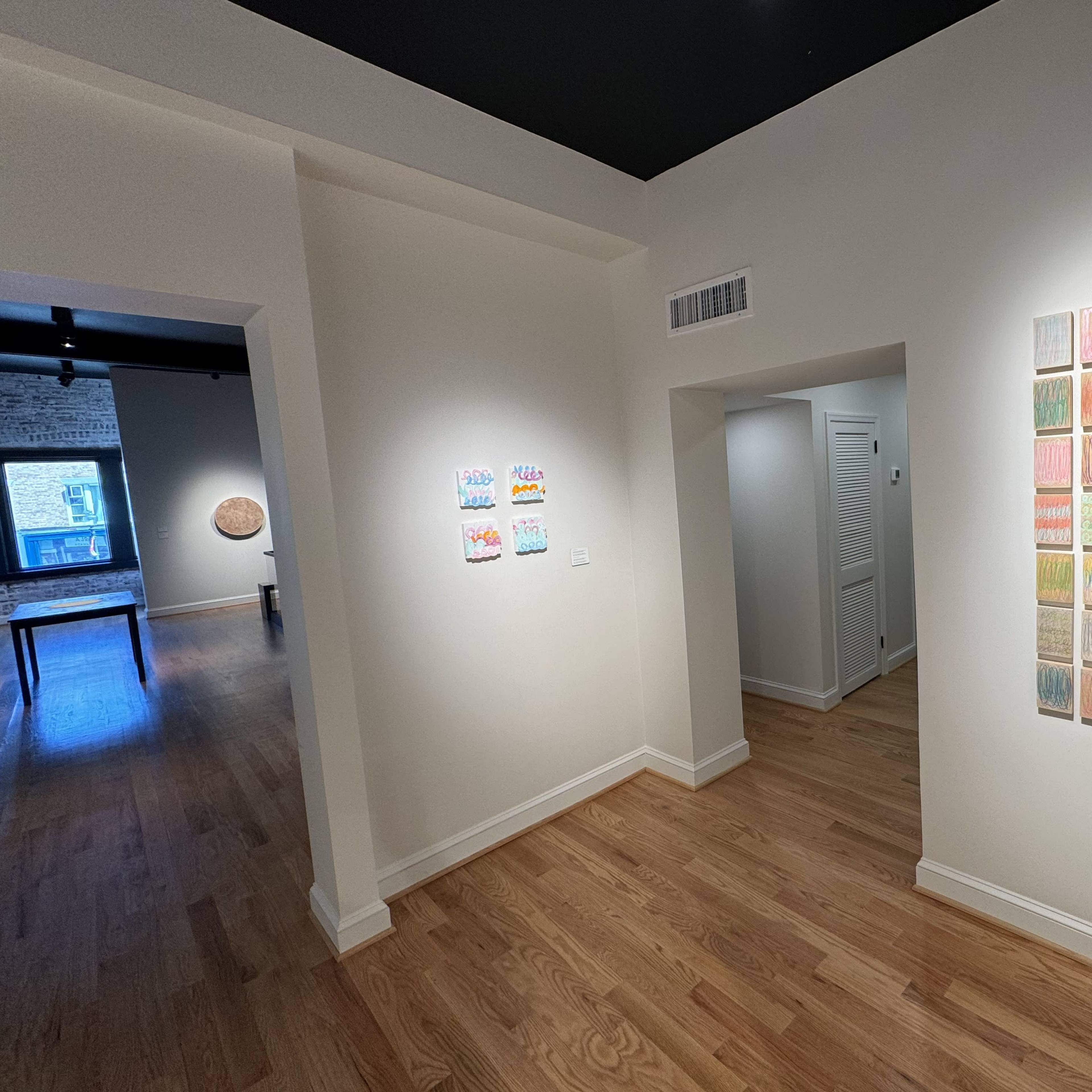 An interior view of an art gallery featuring artwork on the walls and a wooden floor.