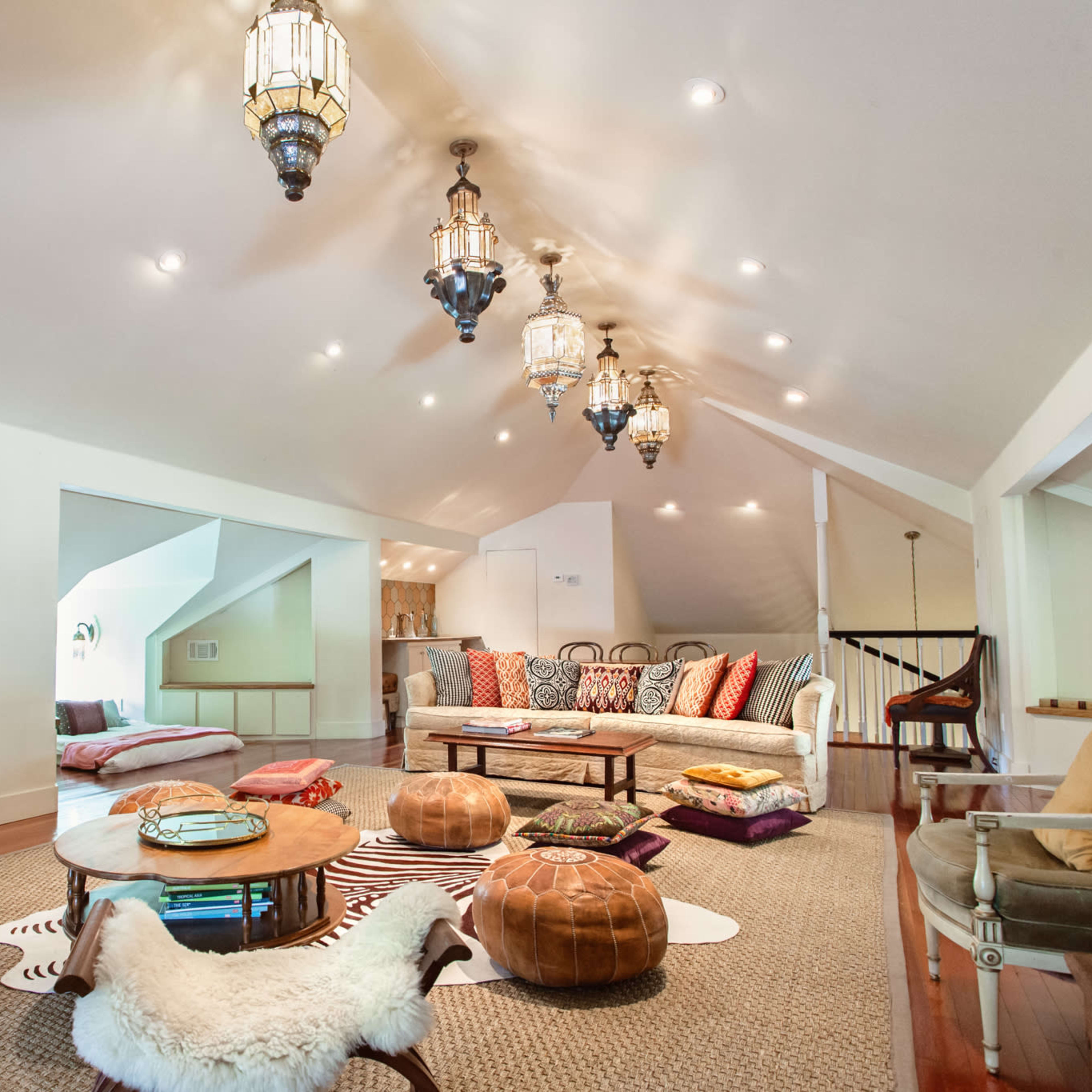 A spacious attic living area adorned with various seating options, decorative lanterns, and a mix of poufs and rugs on the wooden floor.