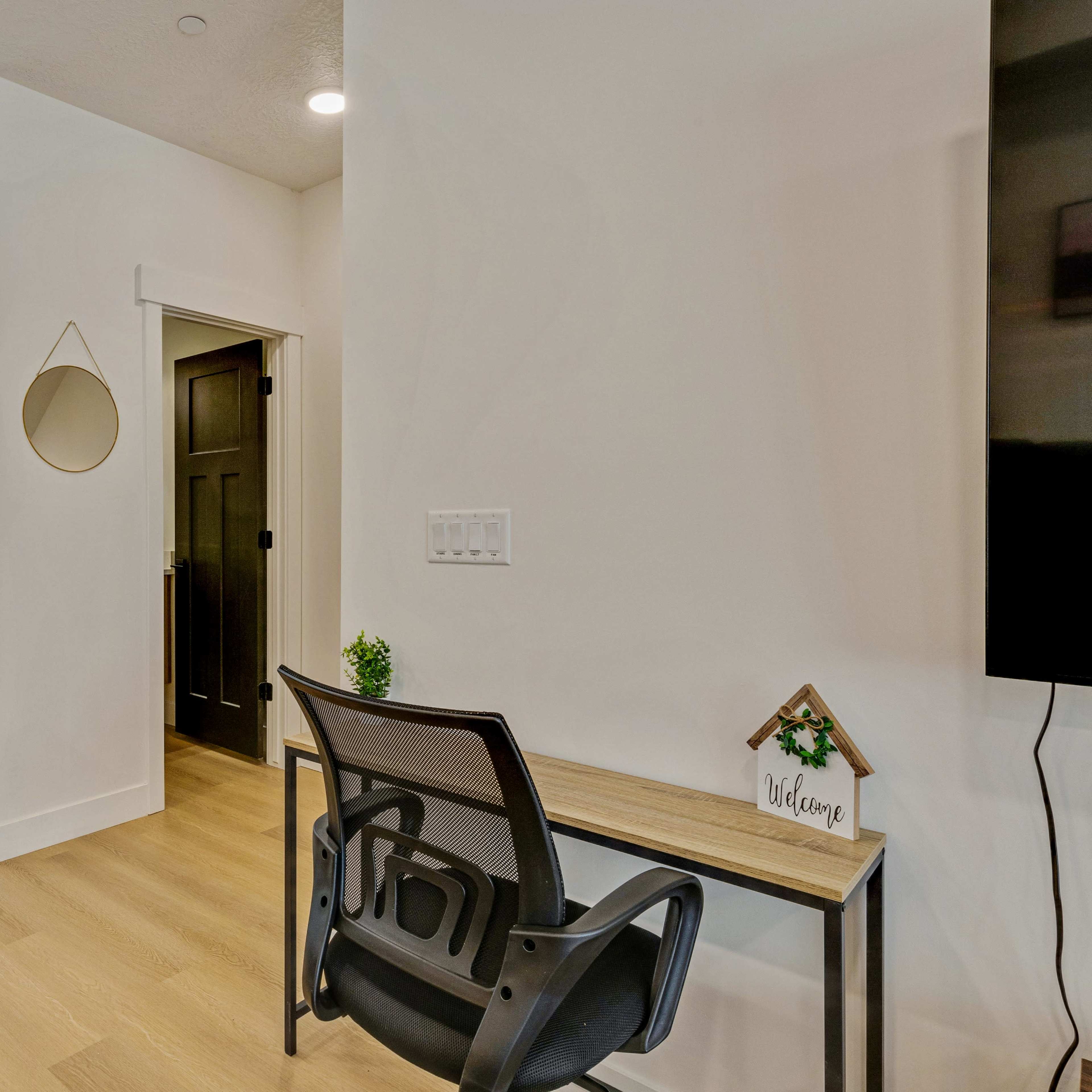 A modern interior space with a dining table and chairs on one side and a desk with a chair against a wall on the other, leading to a doorway.