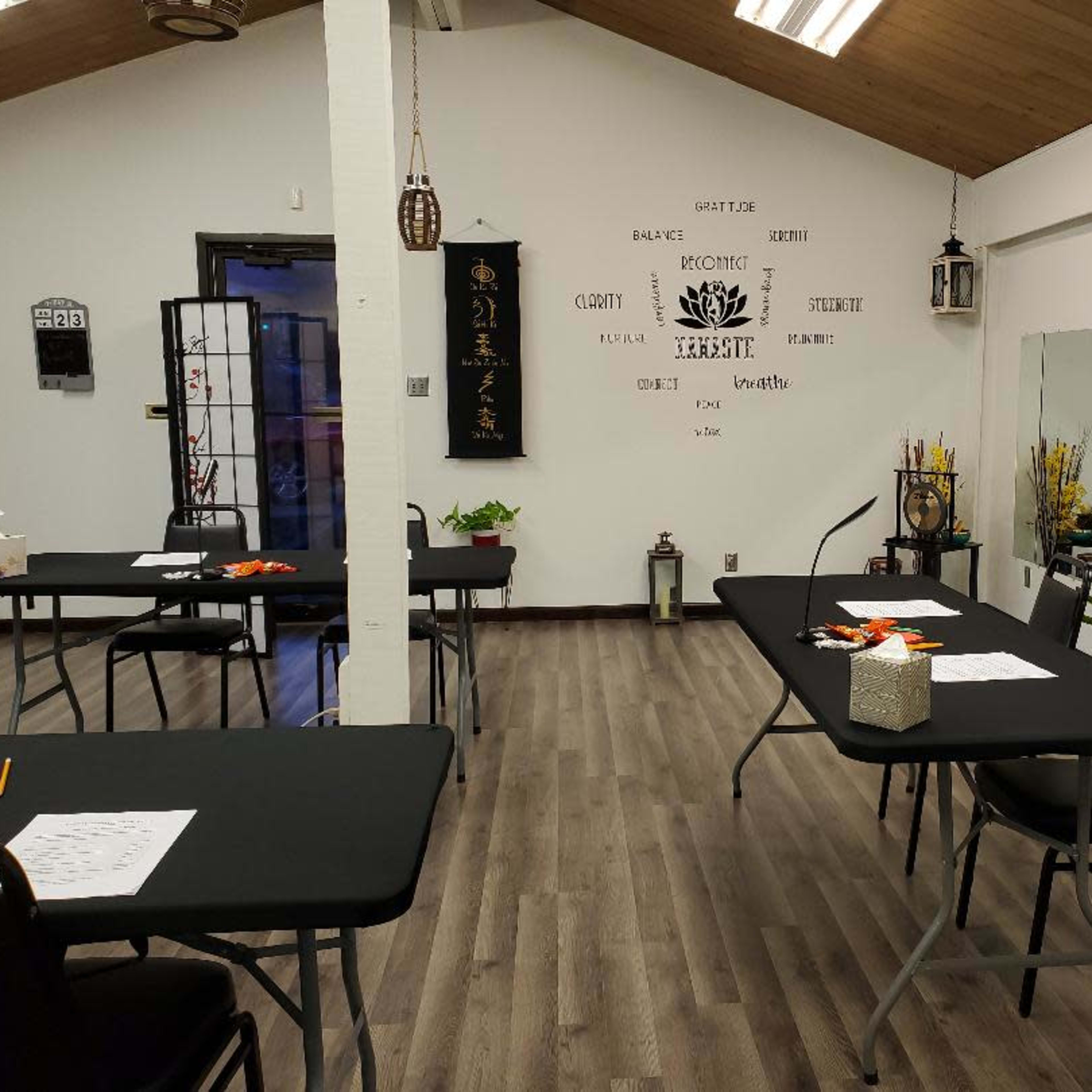 A neatly arranged room with several tables covered in black tablecloths, decorated with plants and lanterns, and featuring a mirror on one wall.