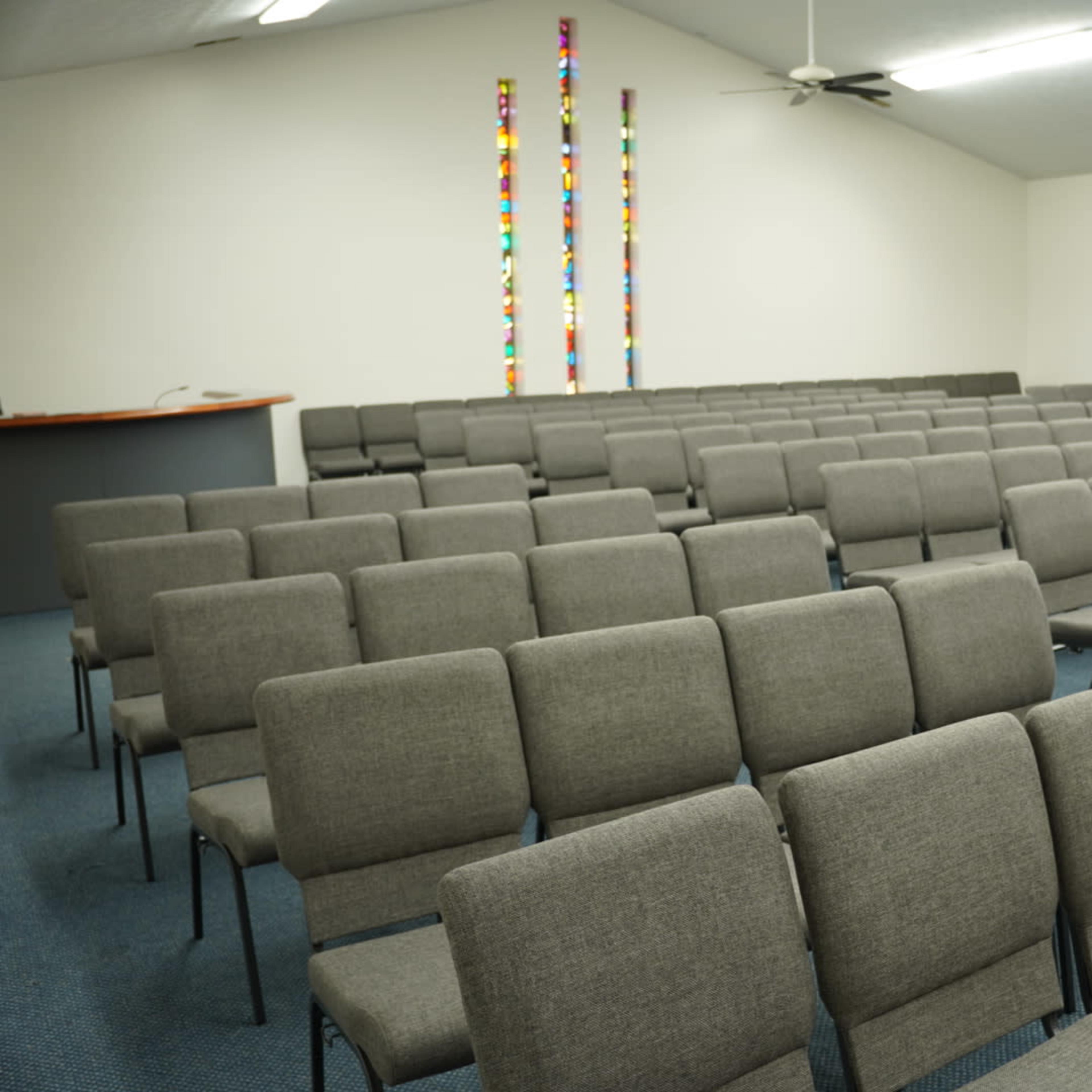 A room with rows of gray chairs arranged for an assembly, with colorful wall decorations in the background.