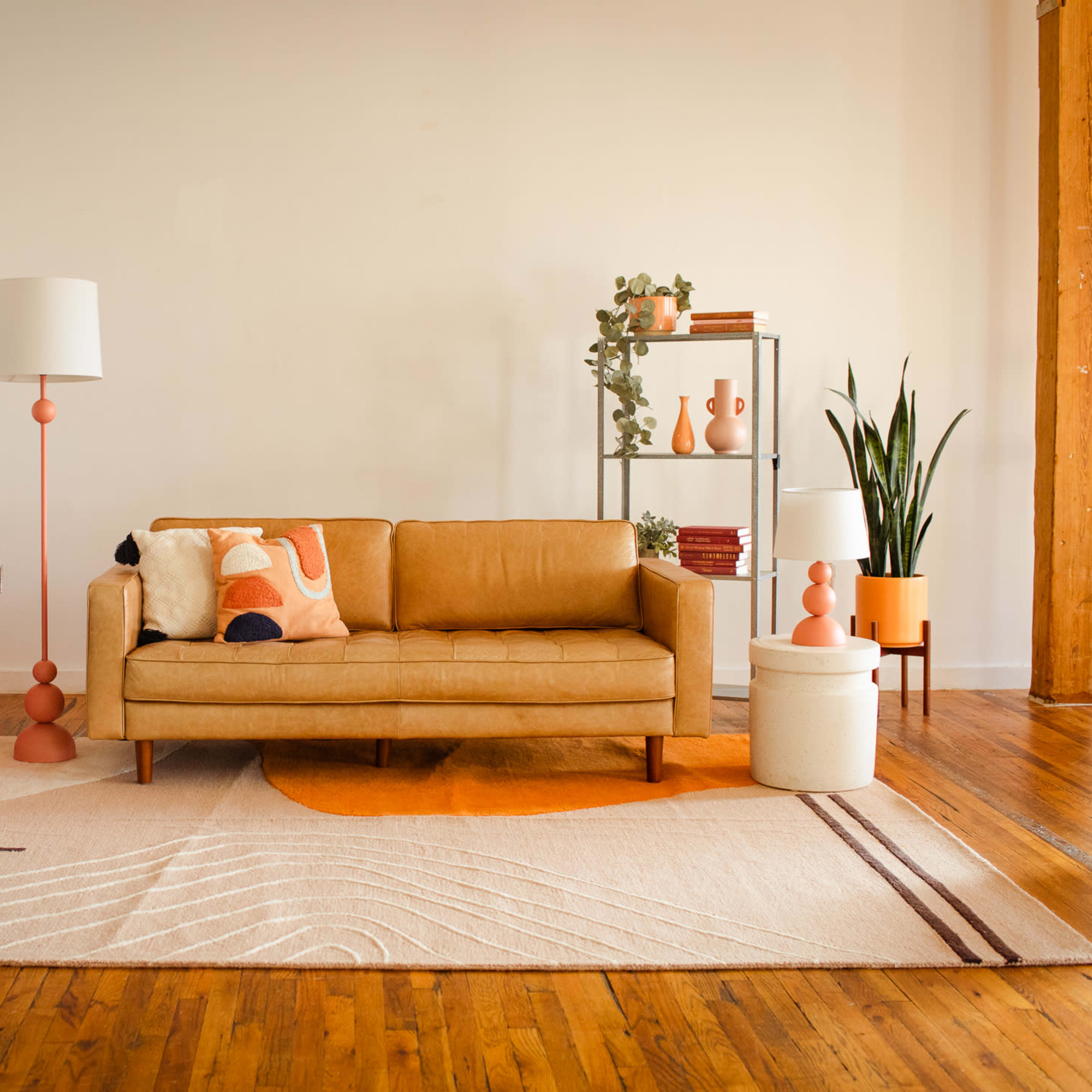 A modern living room featuring a tan sofa, a pink retro refrigerator, decorative plants, and a geometric area rug on wooden floors.