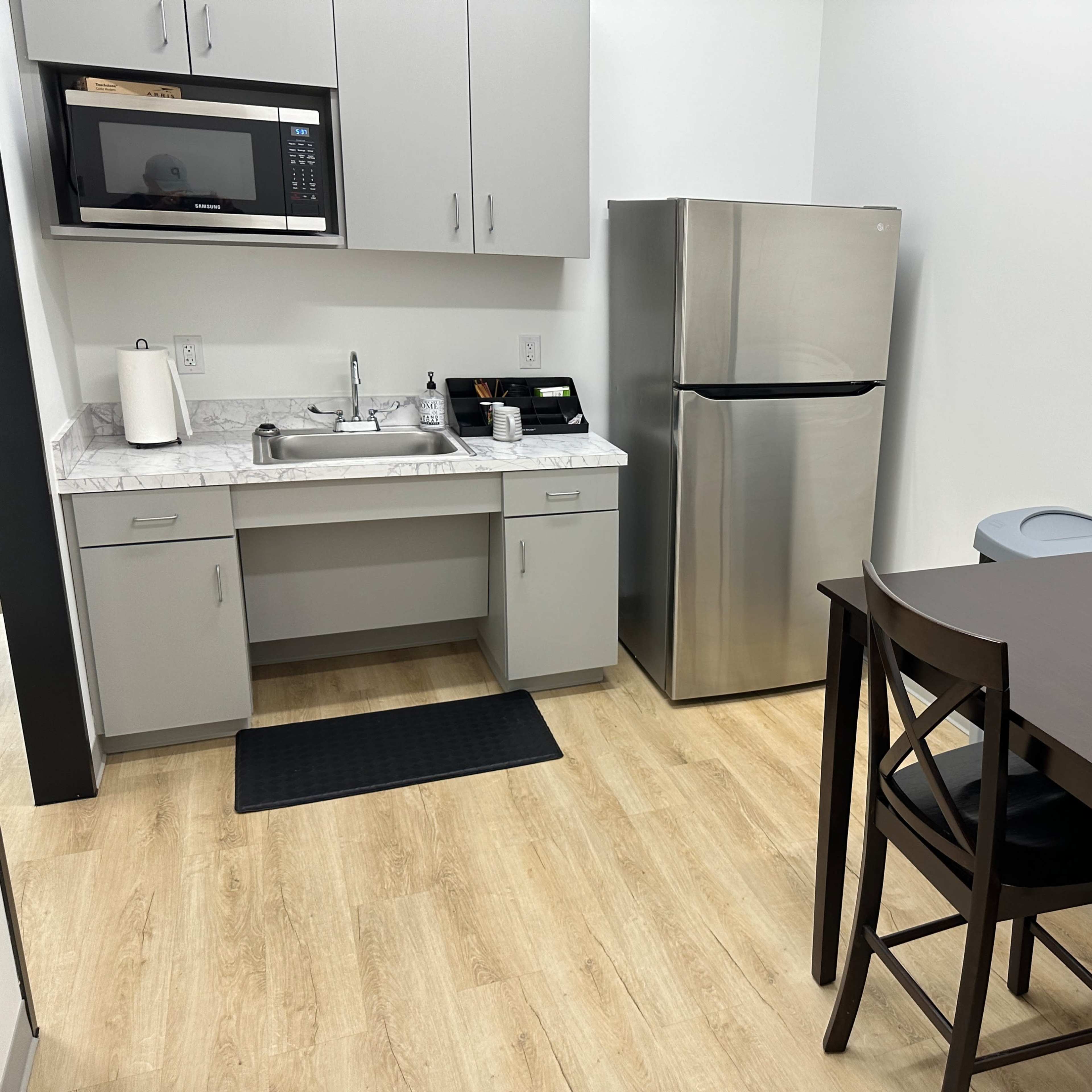 A small kitchen area features a microwave, a stainless steel refrigerator, a sink, and a table with four chairs.