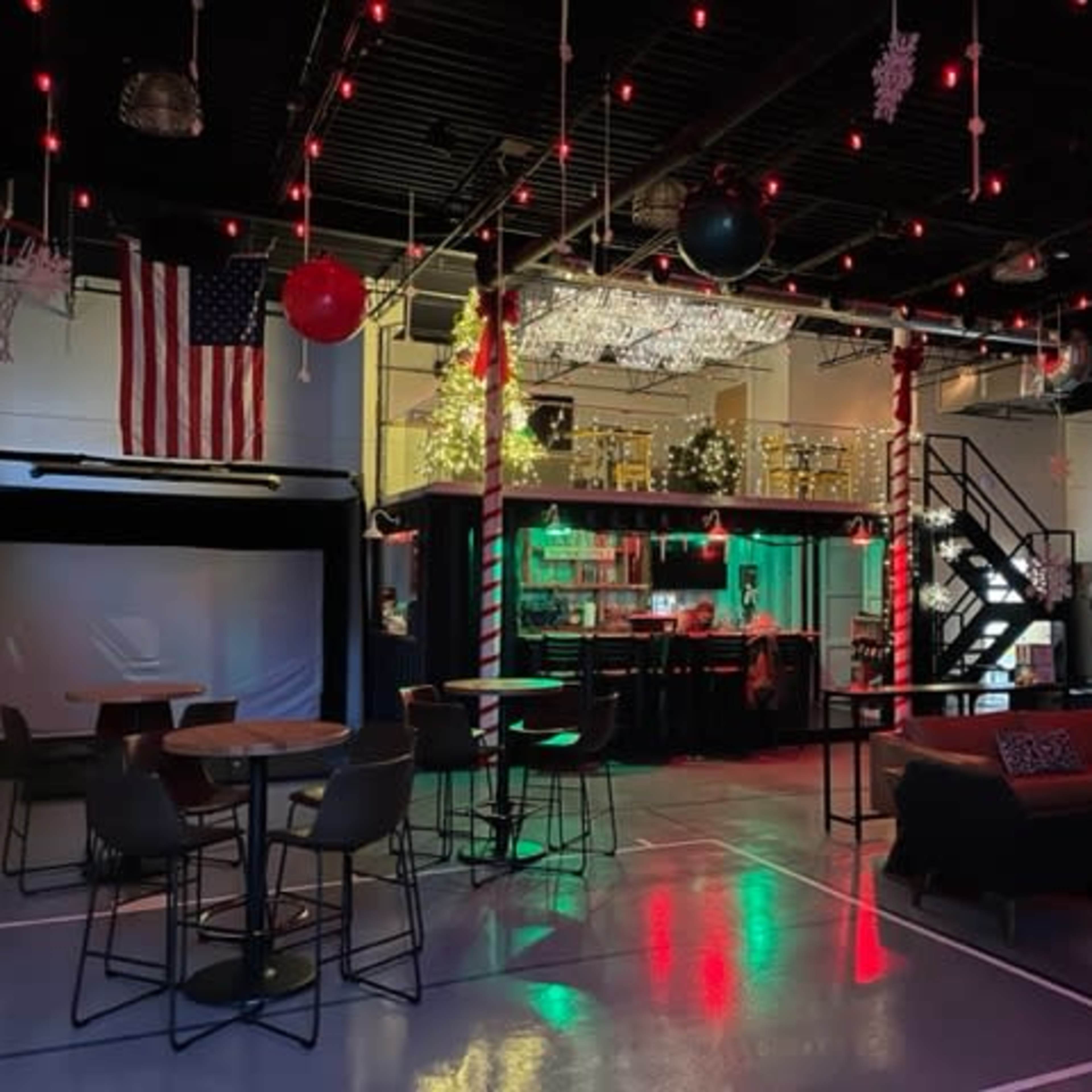 A spacious recreational area featuring a basketball hoop, a golf simulator setup, a large TV, seating arrangements, and a decorative wall.