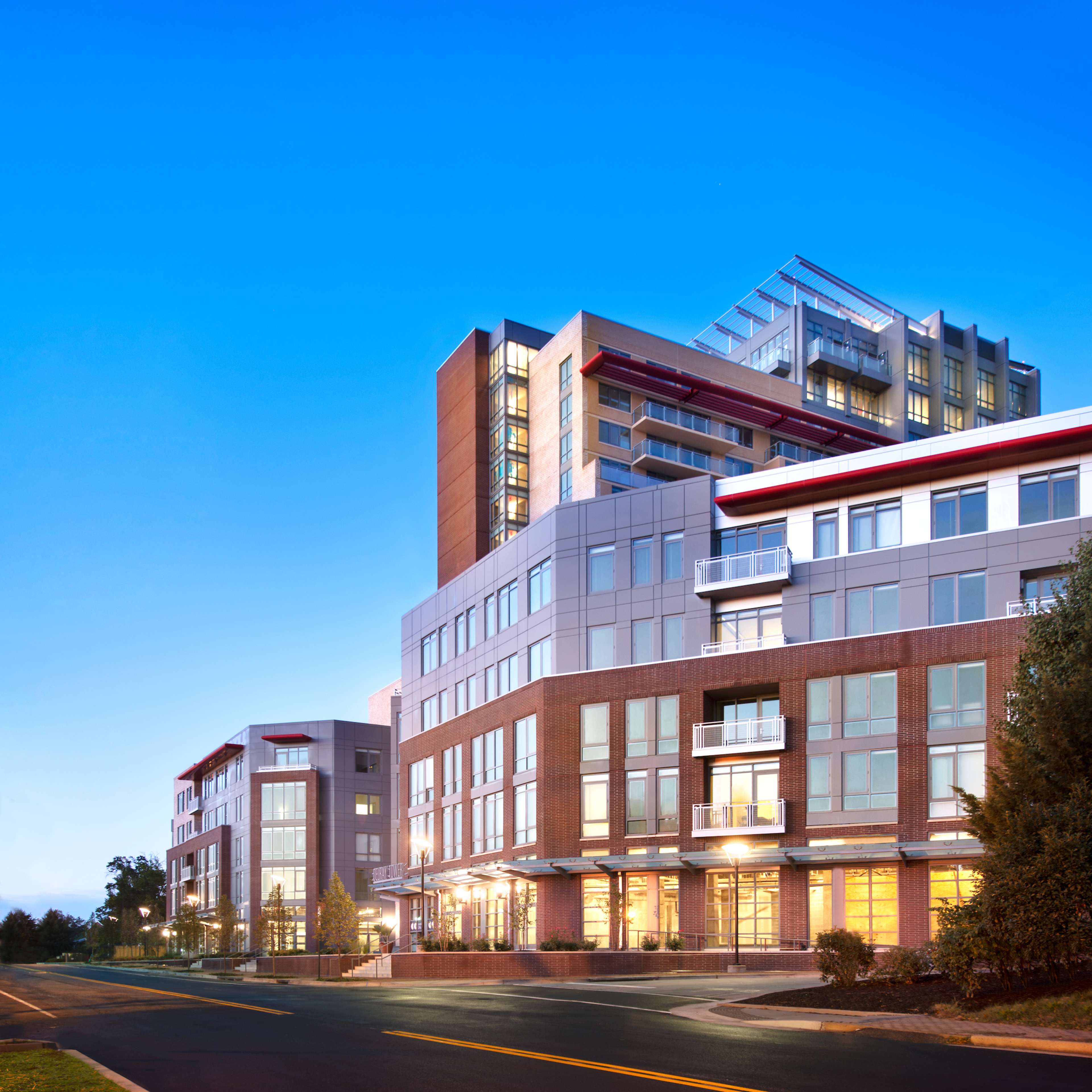 A modern multi-story building complex with a glass and brick facade, located at the intersection of a road.