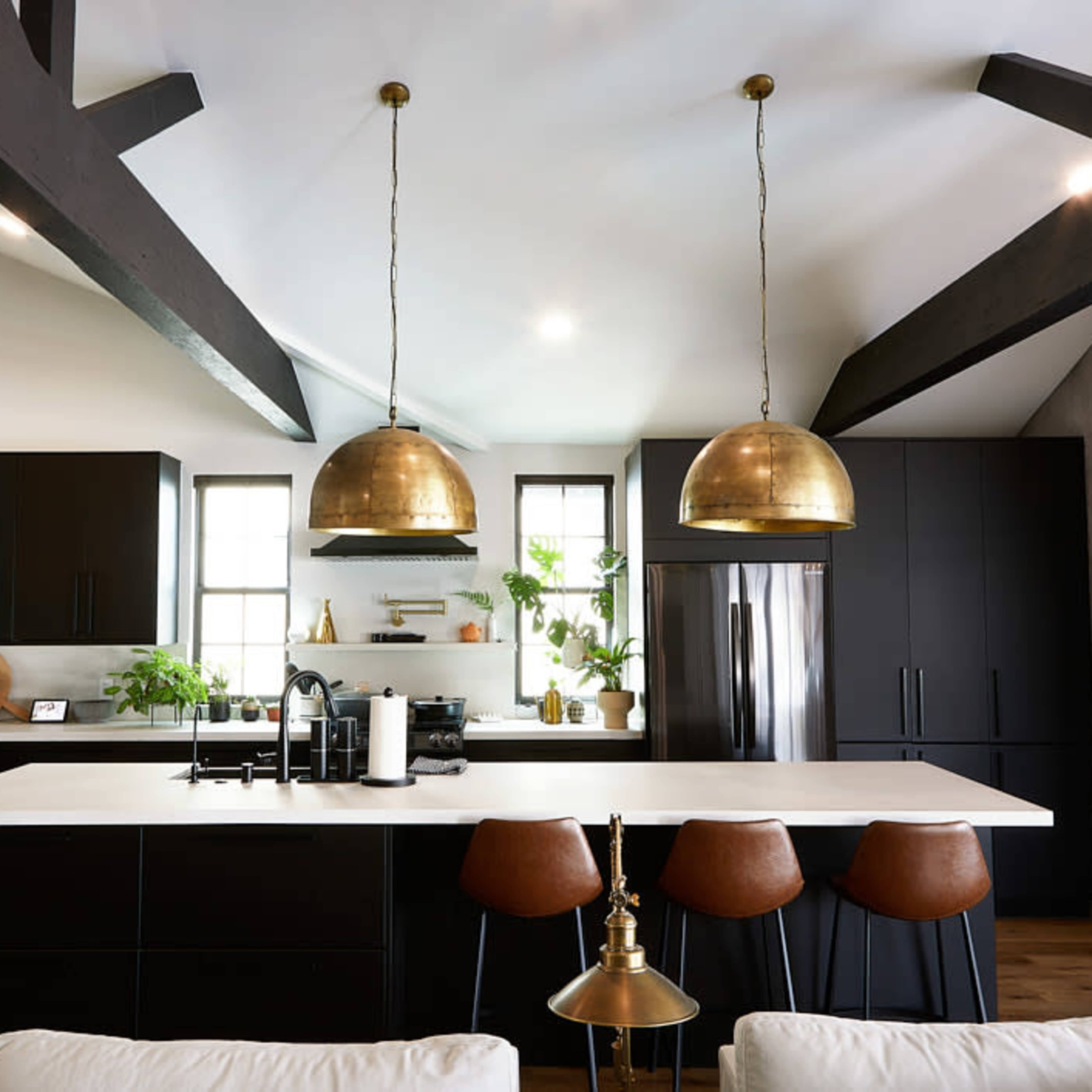 A modern kitchen featuring dark cabinetry, a white countertop, brass pendant lights, and wooden floors.