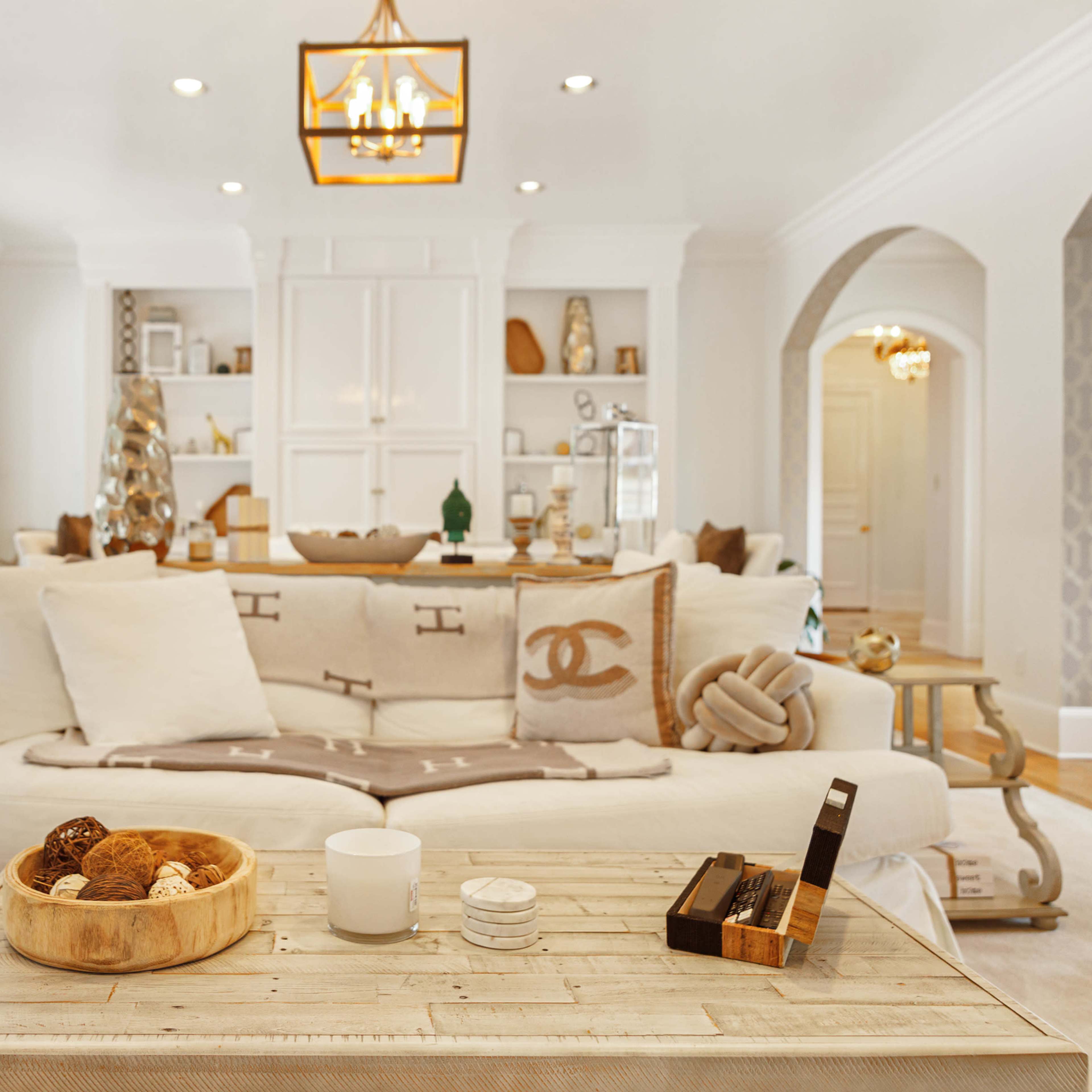 The living room features a sofa adorned with decorative pillows, a coffee table with a wooden bowl and a candle, and an archway leading to another space.