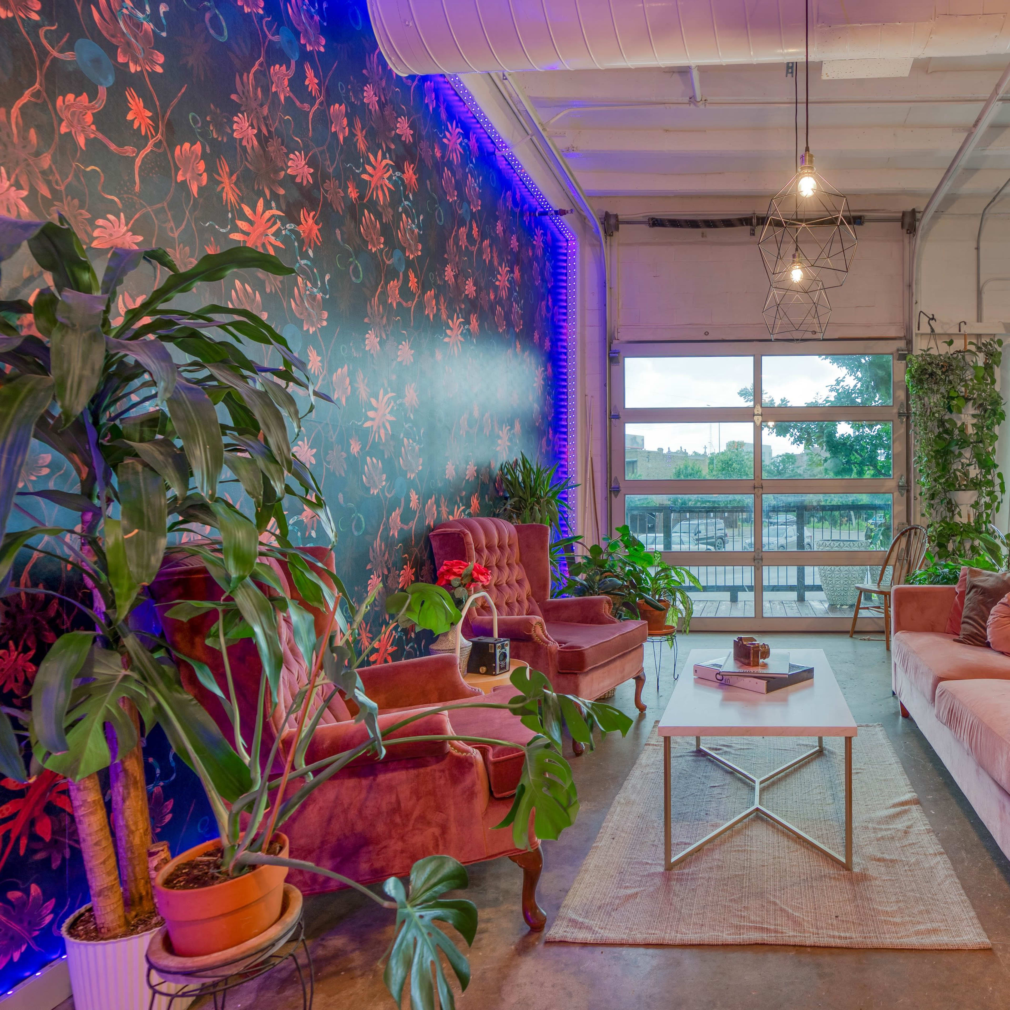 A stylish lounge area with pink velvet furniture, a patterned floral wall, and large windows that allow natural light to fill the space.