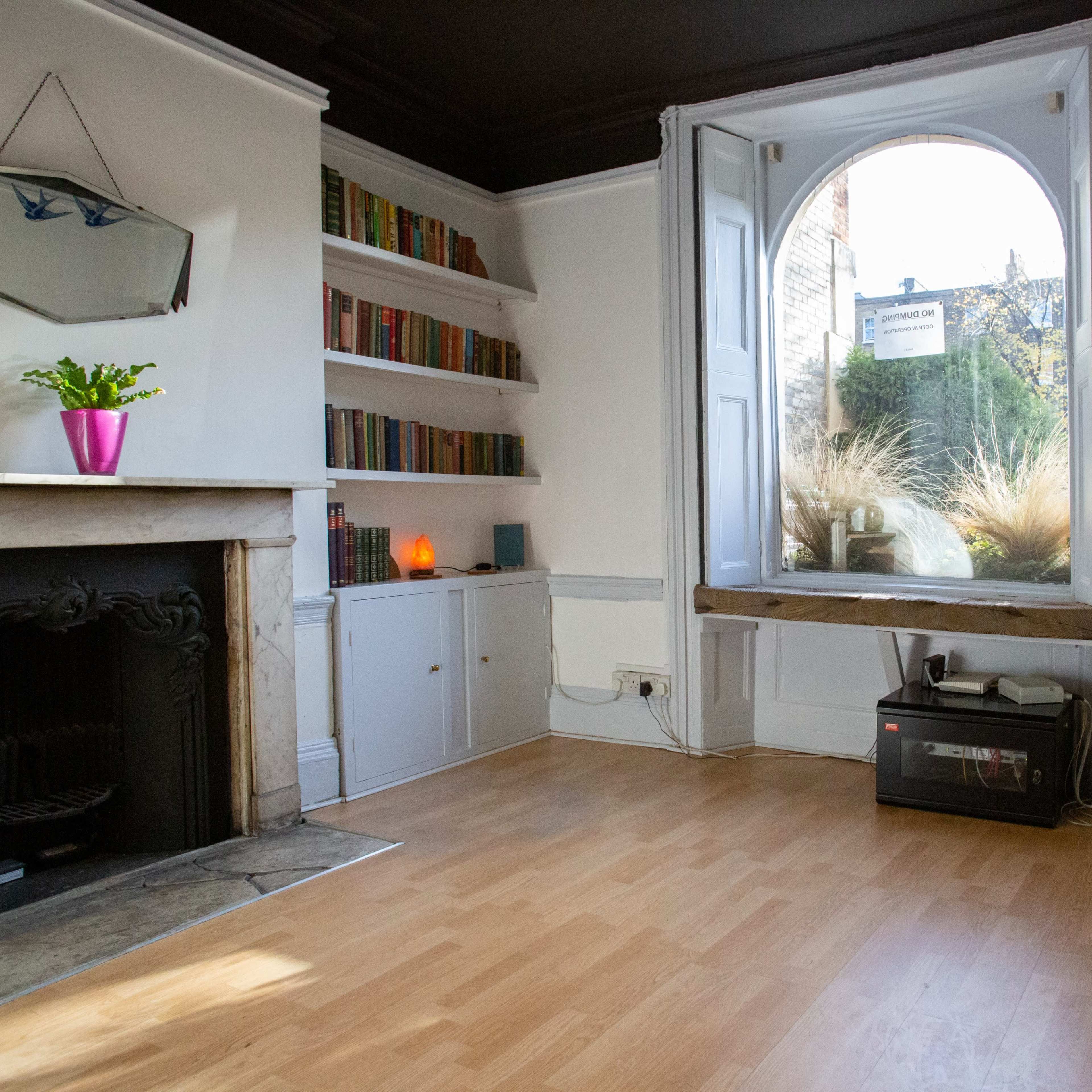 A well-lit room with a large window, a fireplace, built-in bookshelves, and wooden flooring.