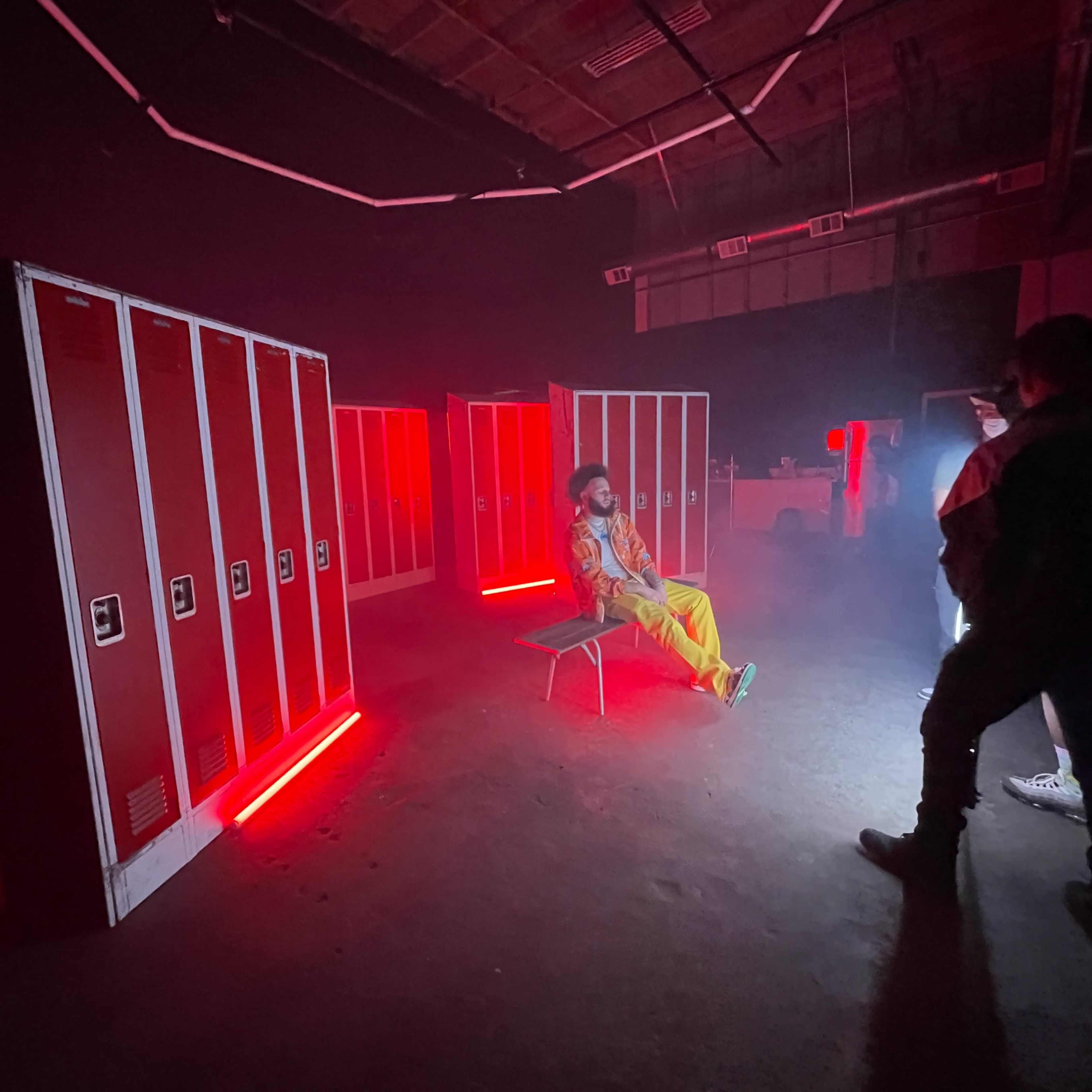 A person sits on a bench in a dimly lit room surrounded by illuminated lockers.