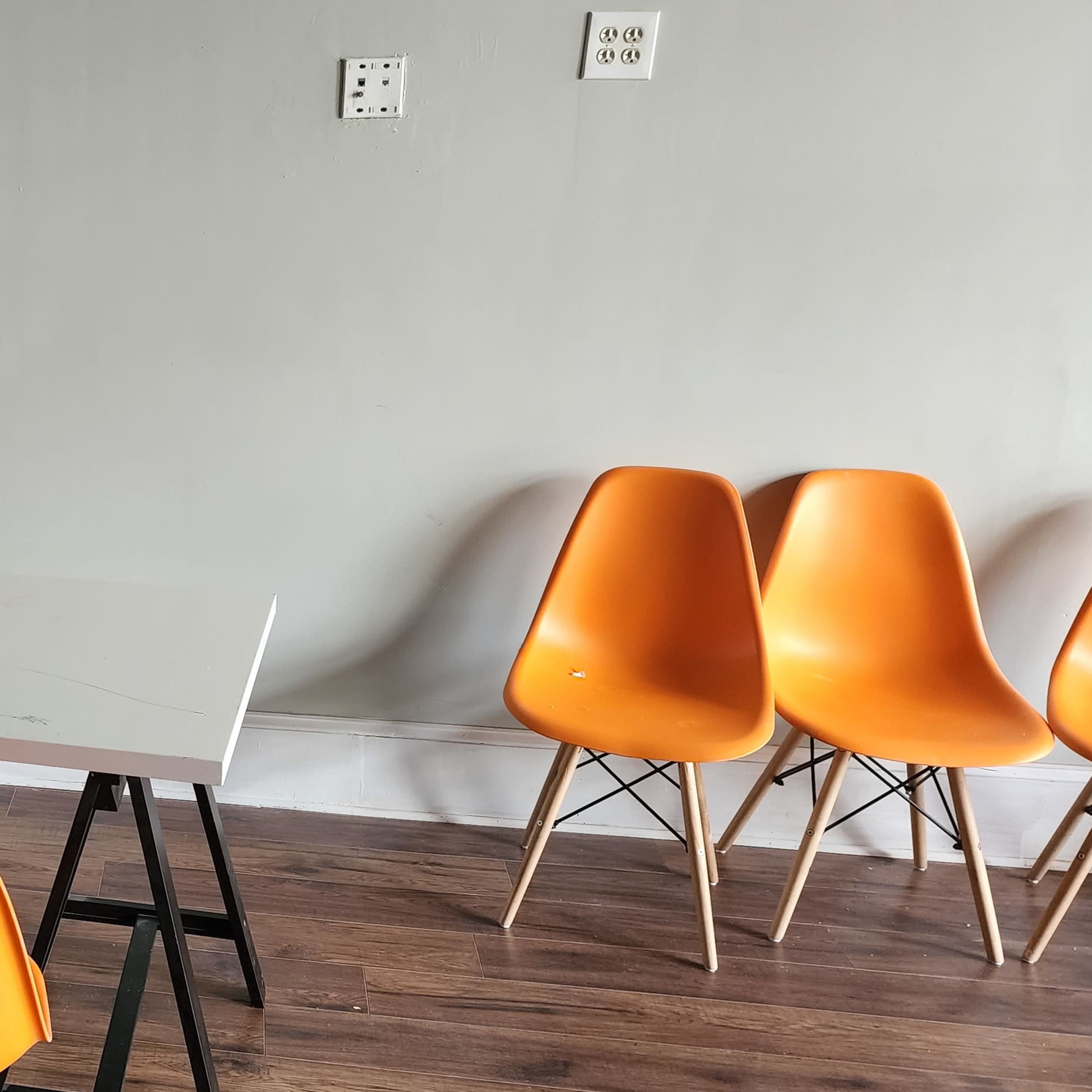 A white table with black legs is placed in a room with six orange chairs arranged around it.