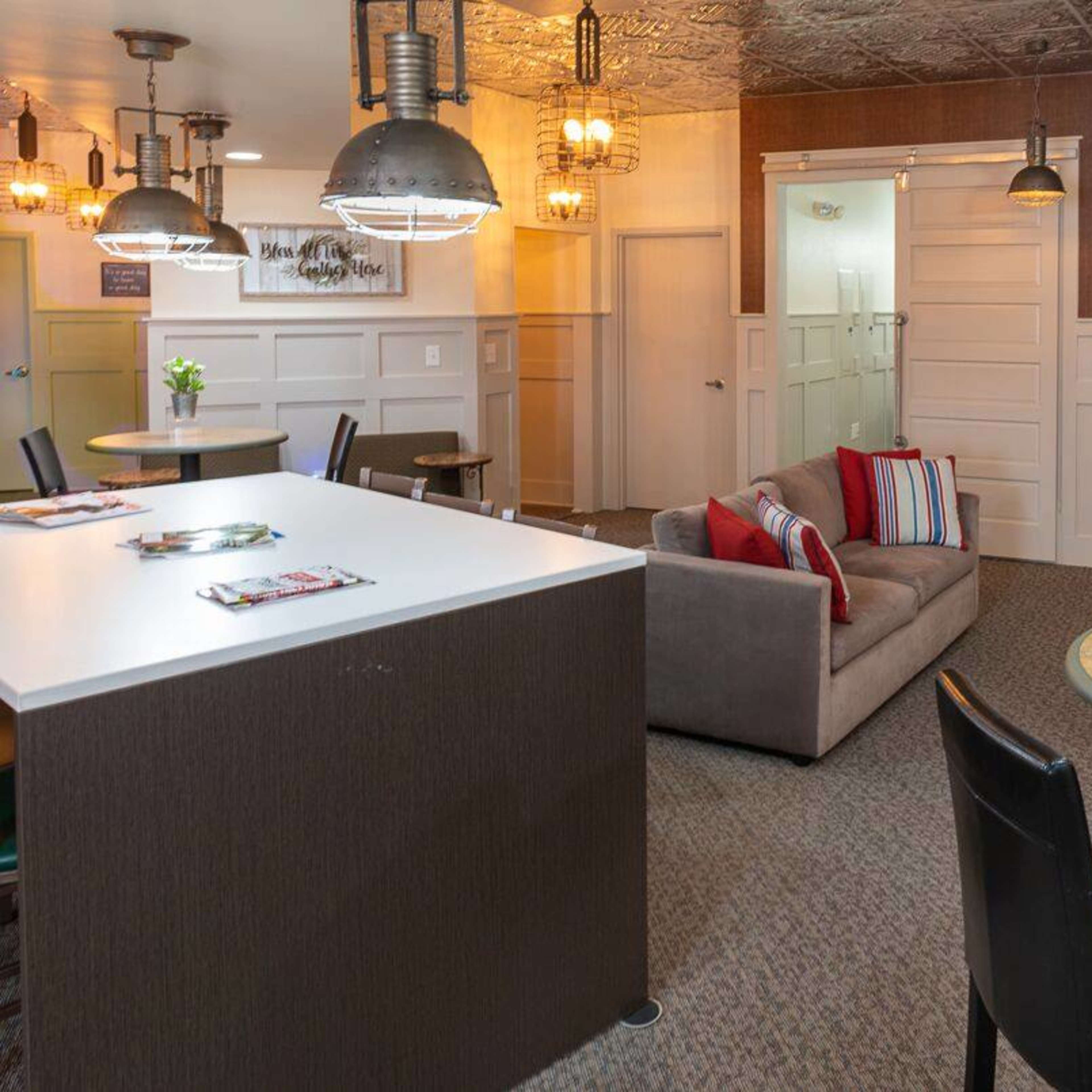 A modern lounge area featuring a gray sofa, two round tables with black chairs, and pendant lighting.